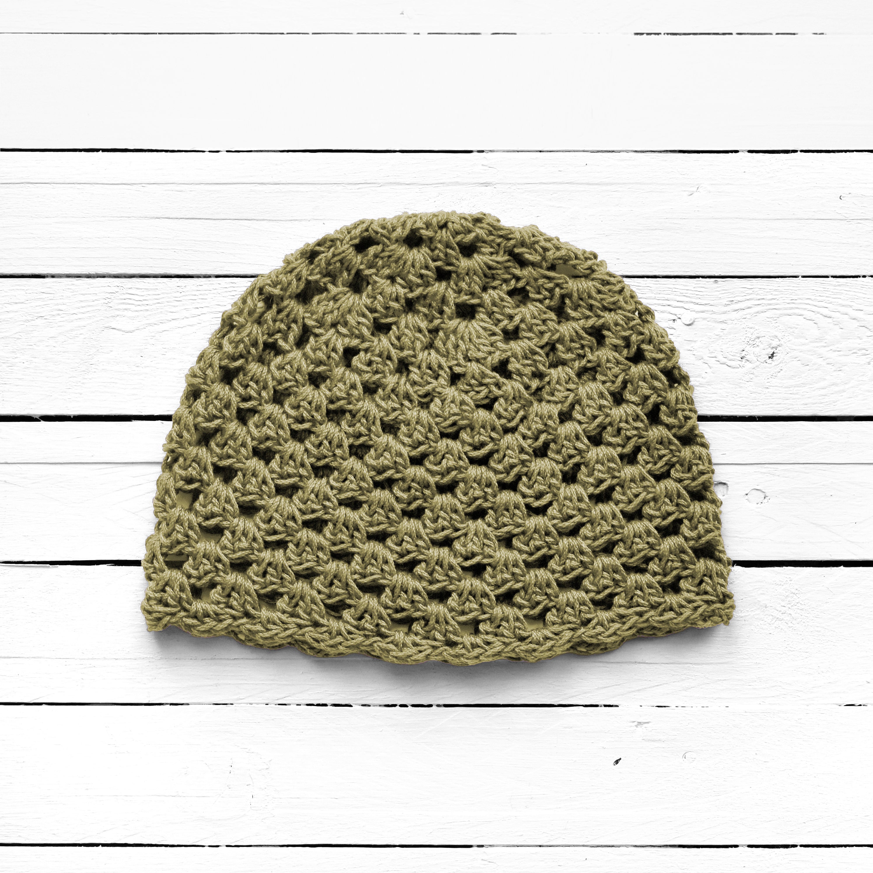 Sage green crochet beanie on a white wooden surface.
