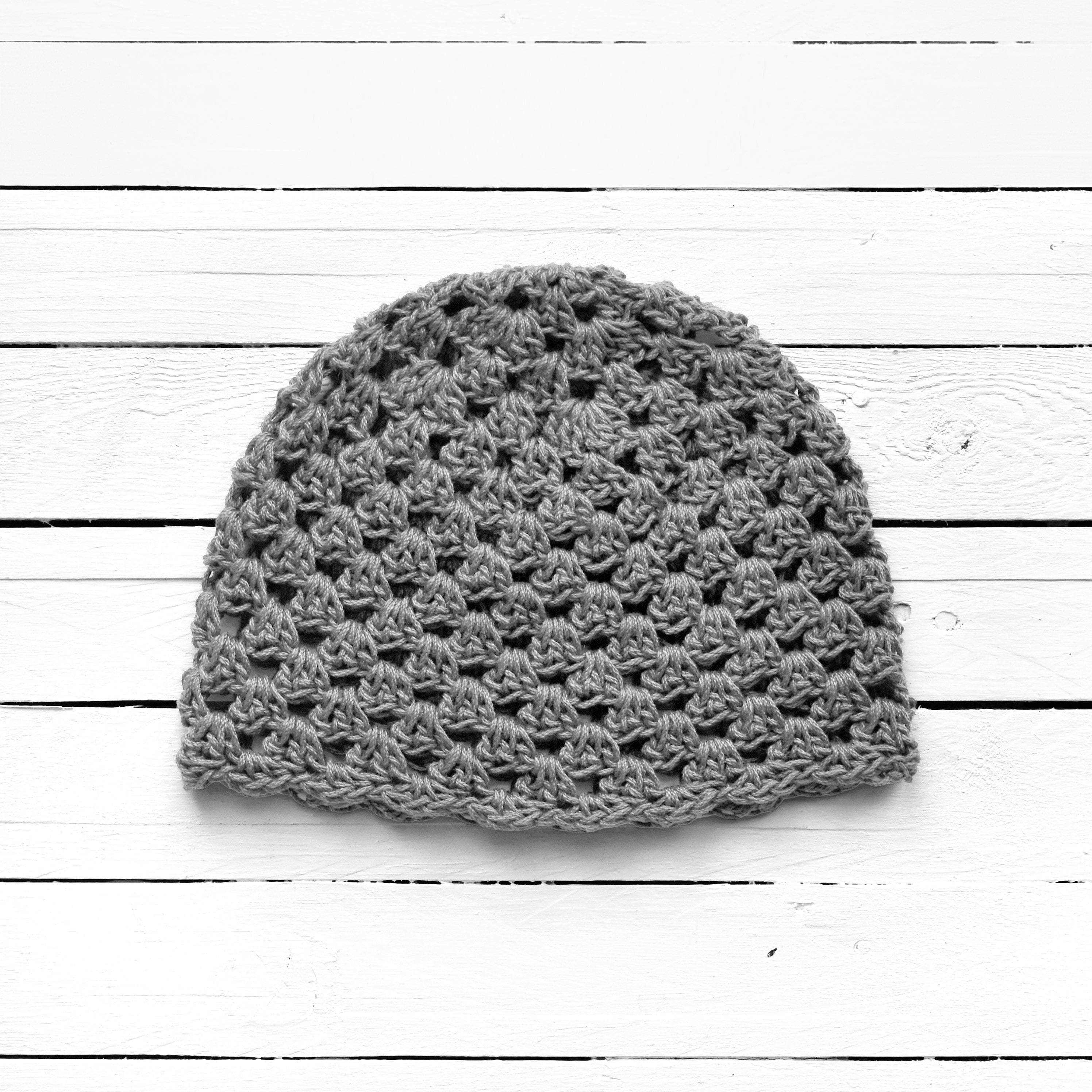 Gray crochet beanie on a white wooden surface.