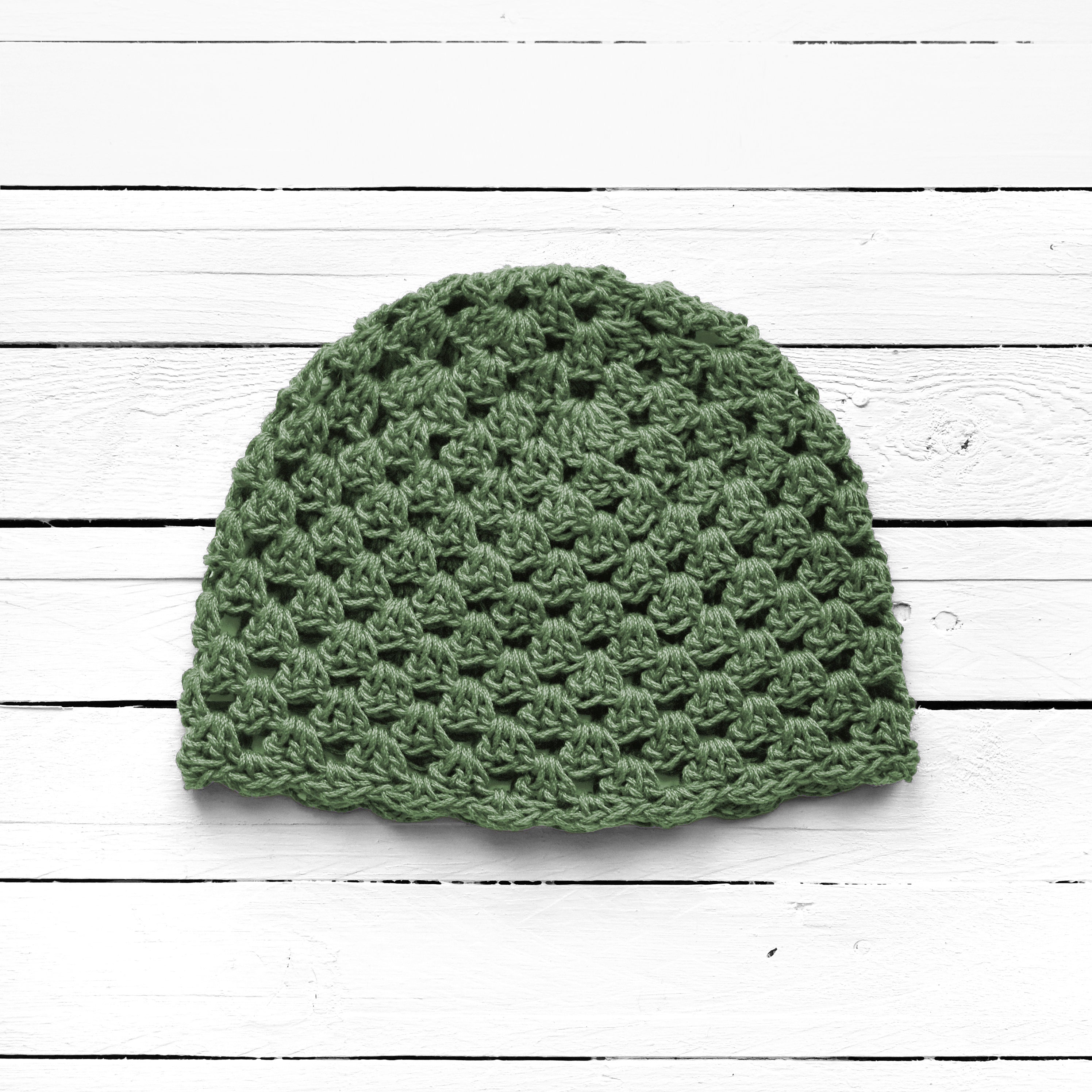 Earthy green crochet hat on a white wooden surface.