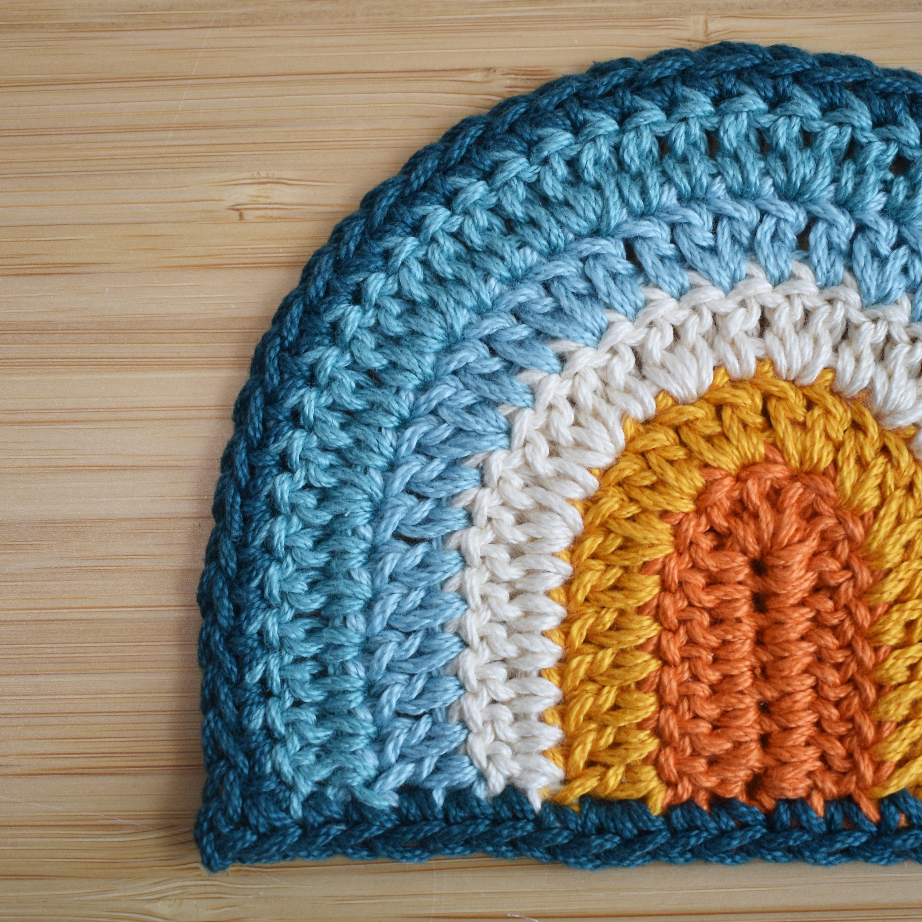 Crocheted rainbow with blue, orange, and yellow colors on a wooden surface.