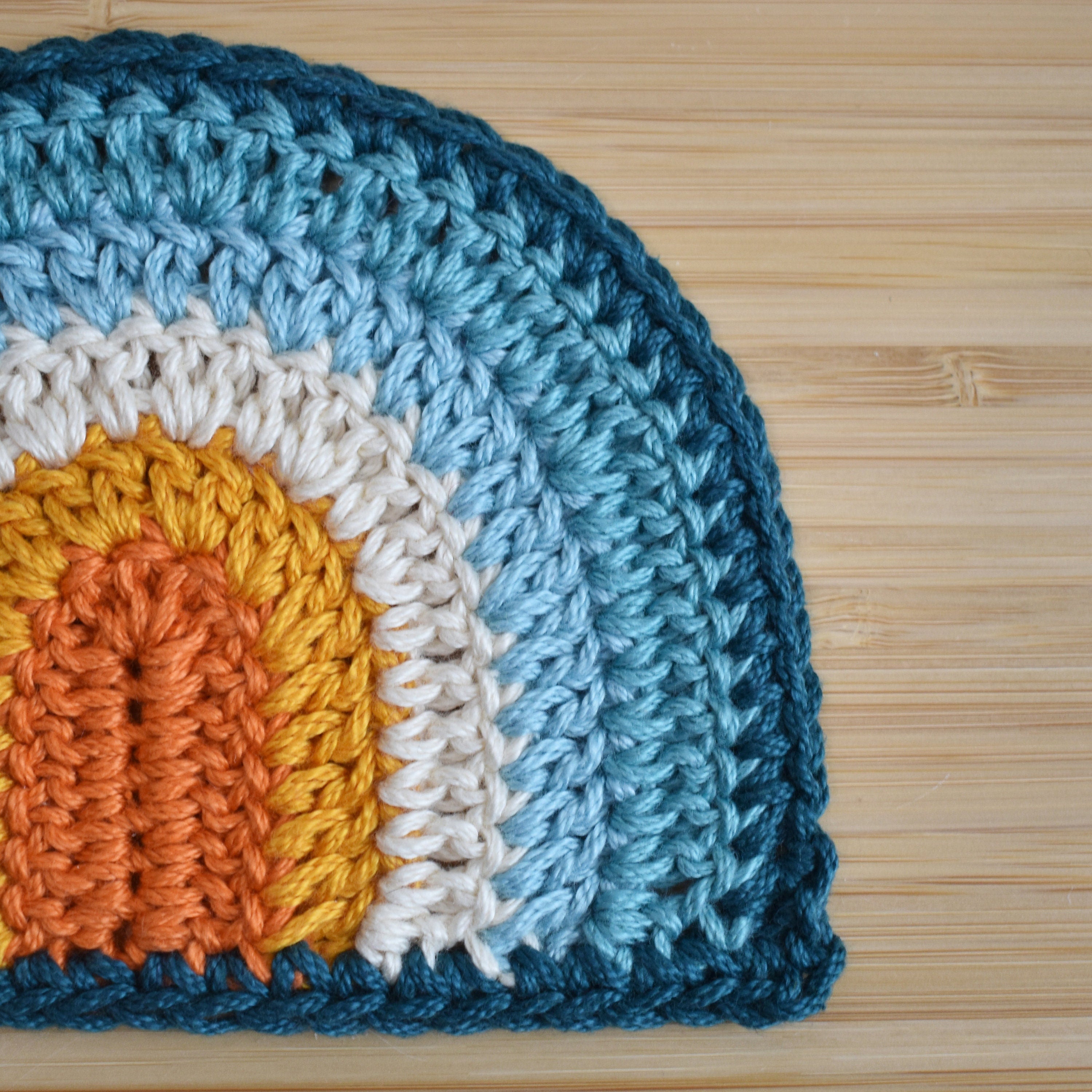 Close-up of a crocheted rainbow with blue, orange, and white colors on a wooden surface.