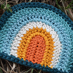 Crocheted rainbow coaster with a blue and orange color pattern on the grass.