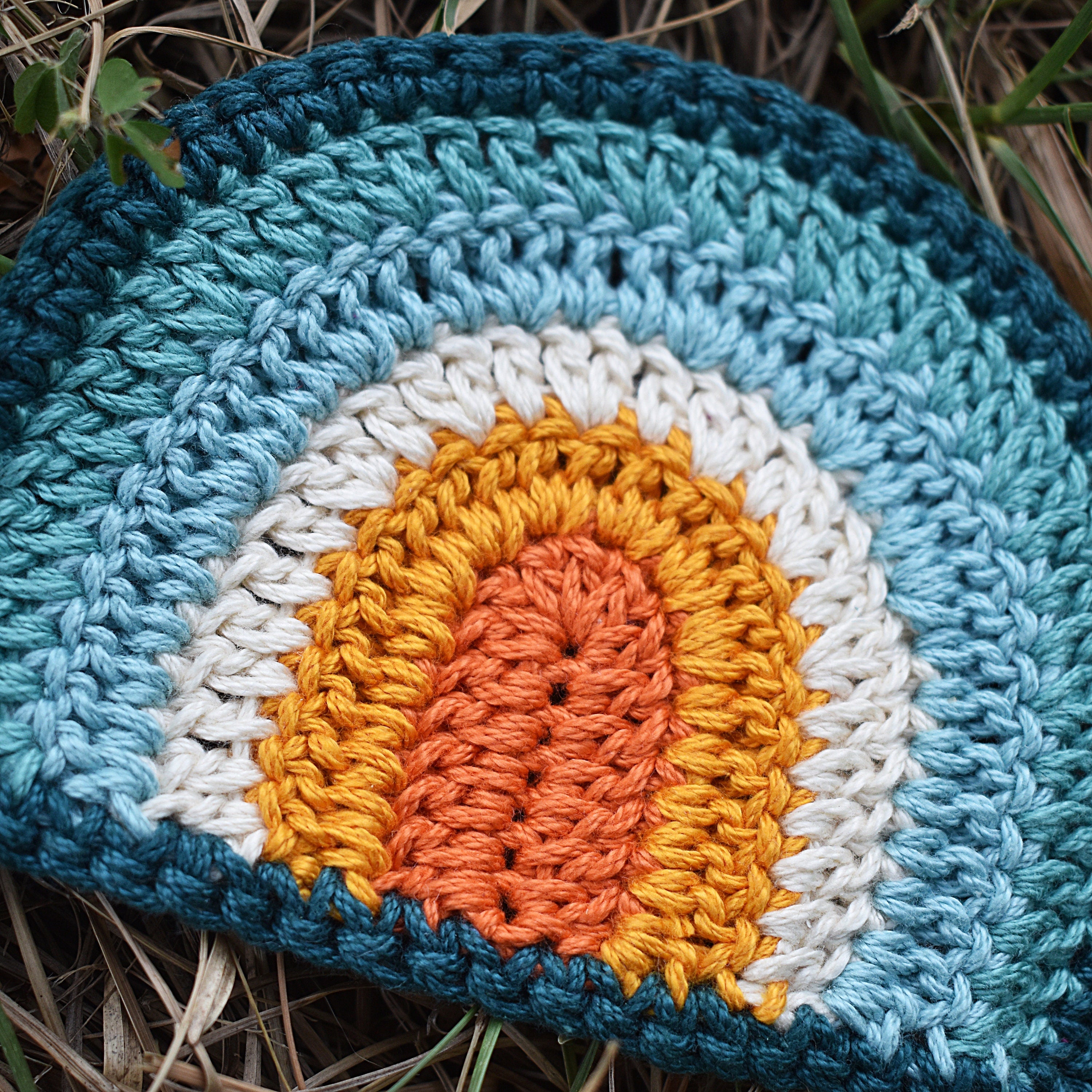 Crocheted rainbow coaster with a blue and orange color pattern on the grass.