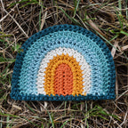 Crocheted rainbow patch on a grassy background.