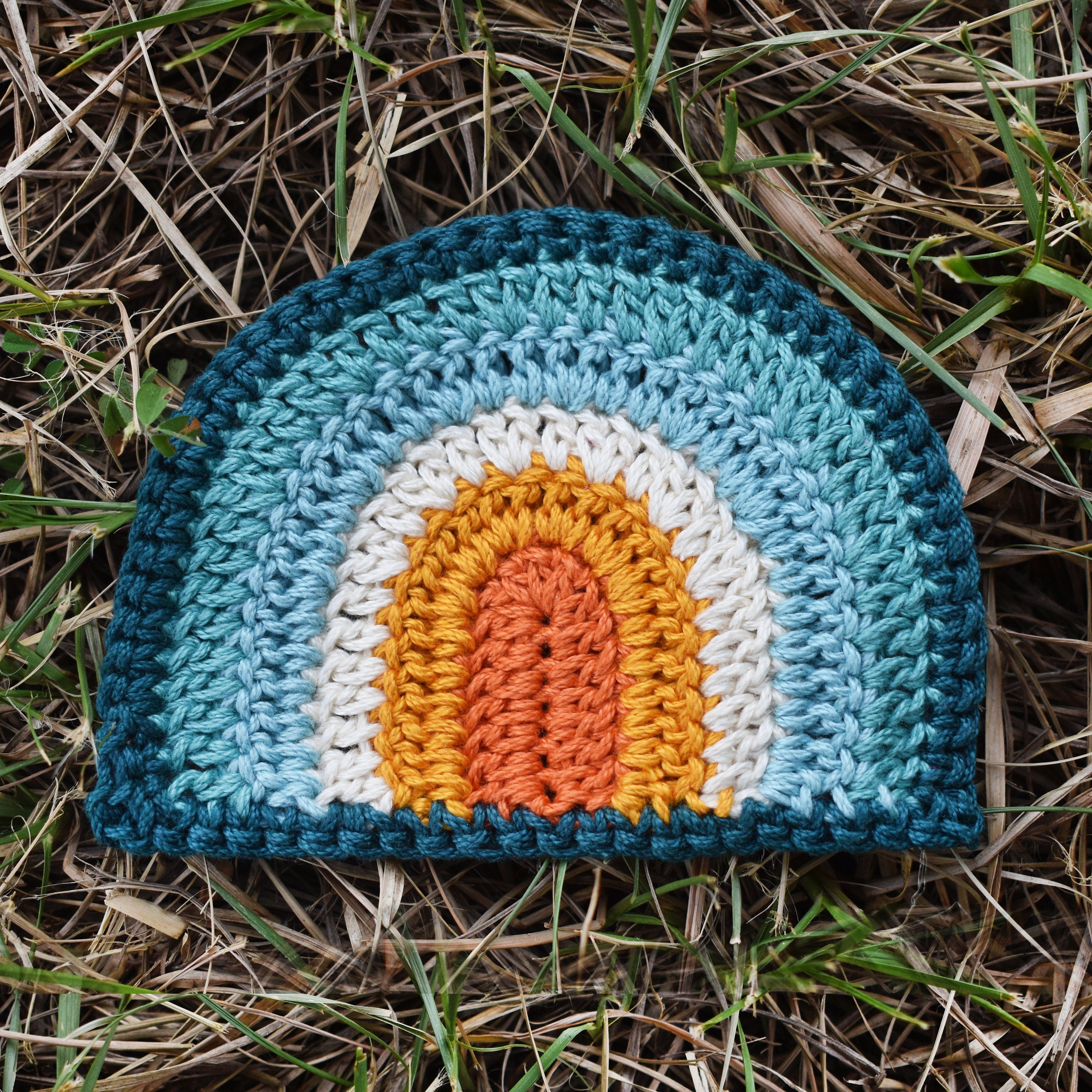 Crocheted rainbow patch on a grassy background.
