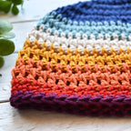 Close-up of a olorful crocheted beanie with a striped pattern on a wooden surface.