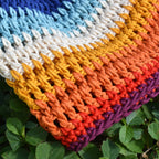 Close-up of a colorful crocheted hat with a striped pattern on green leaves.