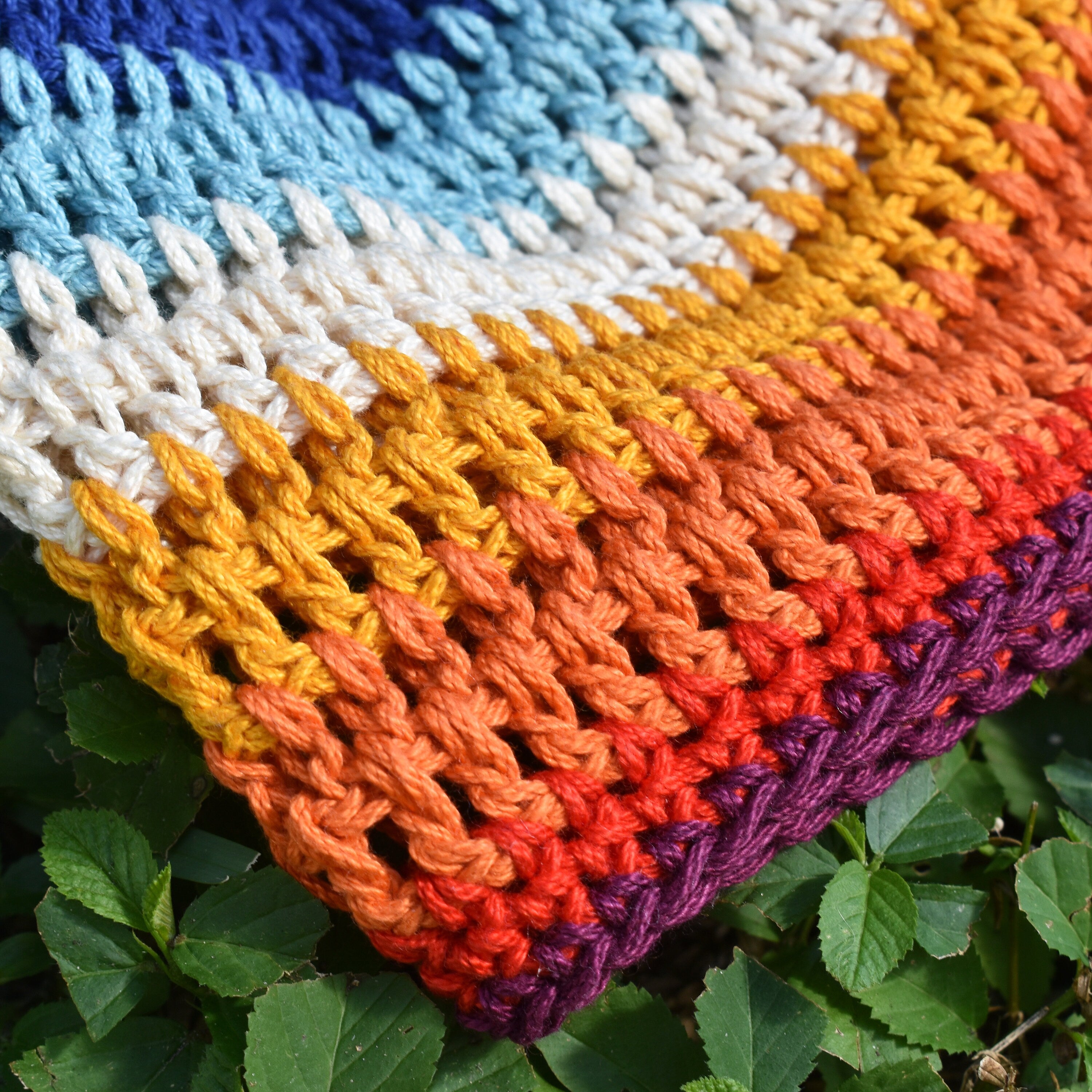 Close-up of a colorful crocheted hat with a striped pattern on green leaves.