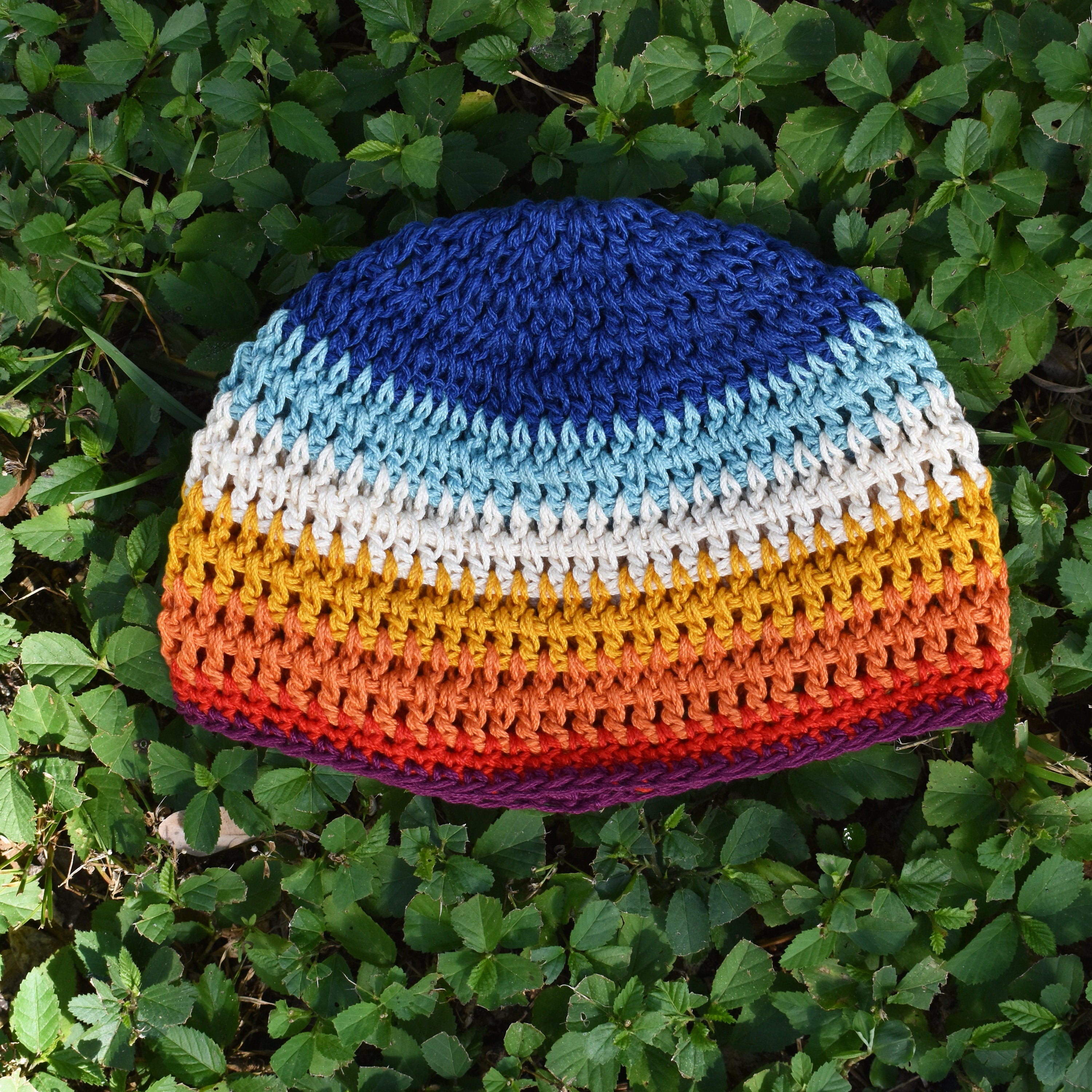 Colorful striped crocheted beanie on green grass.