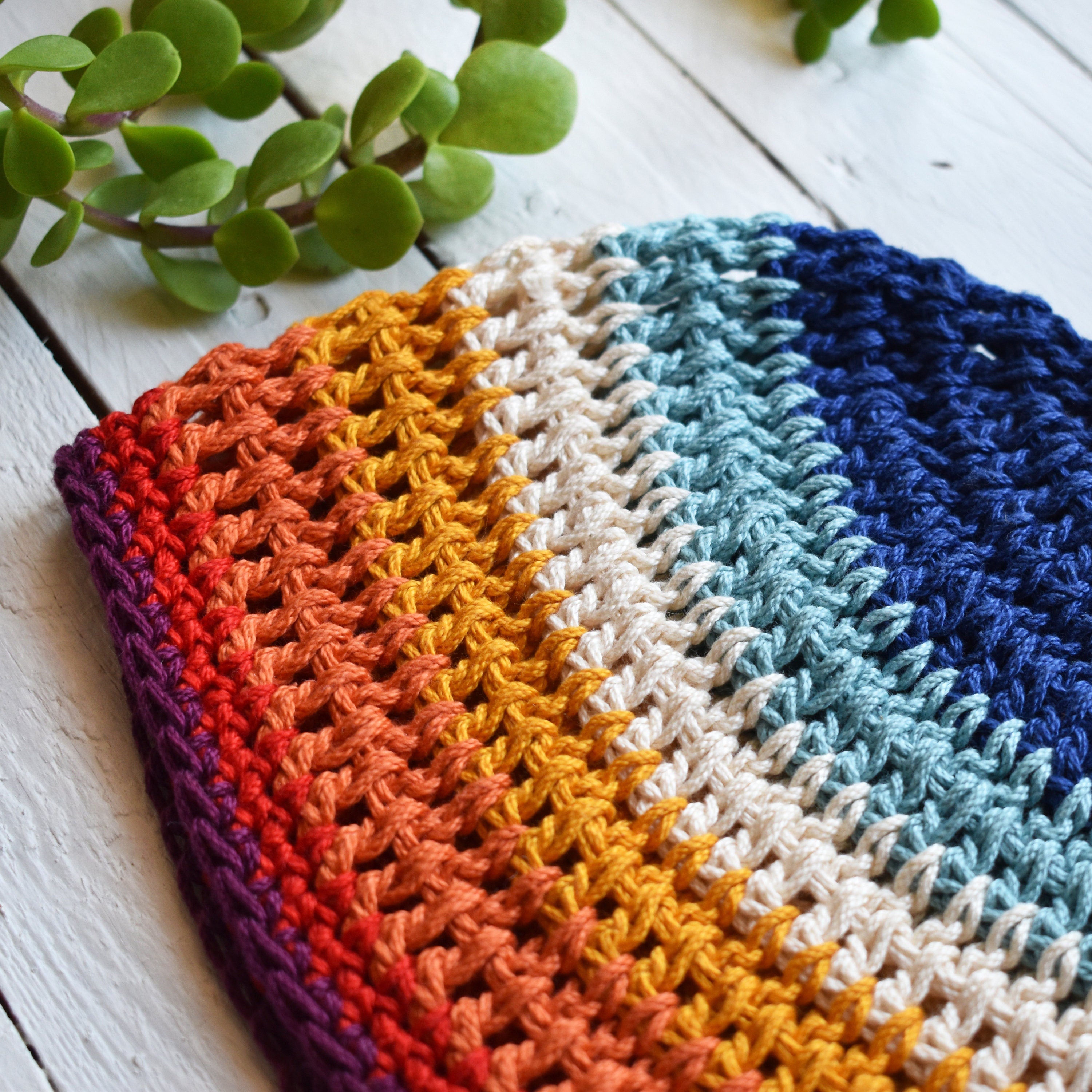 Colorful crocheted beanie with a striped pattern on a white wooden surface.