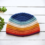 Colorful crocheted beanie on a white wooden surface with green plants.