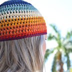 A woman wearing a colorful knitted beanie with a blurred natural background.