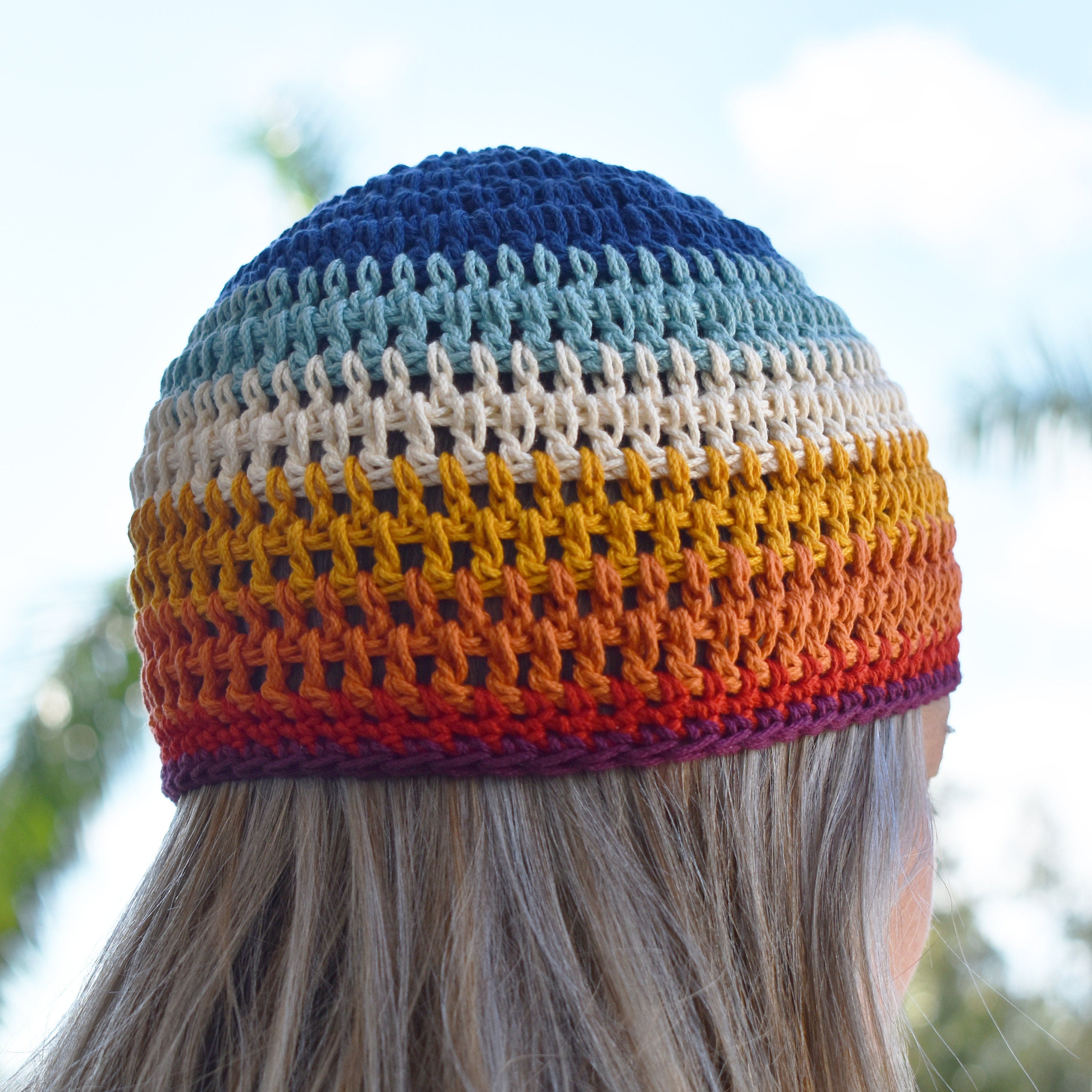A person wearing a colorful striped beanie looks out into the distance of a blurred natural background.