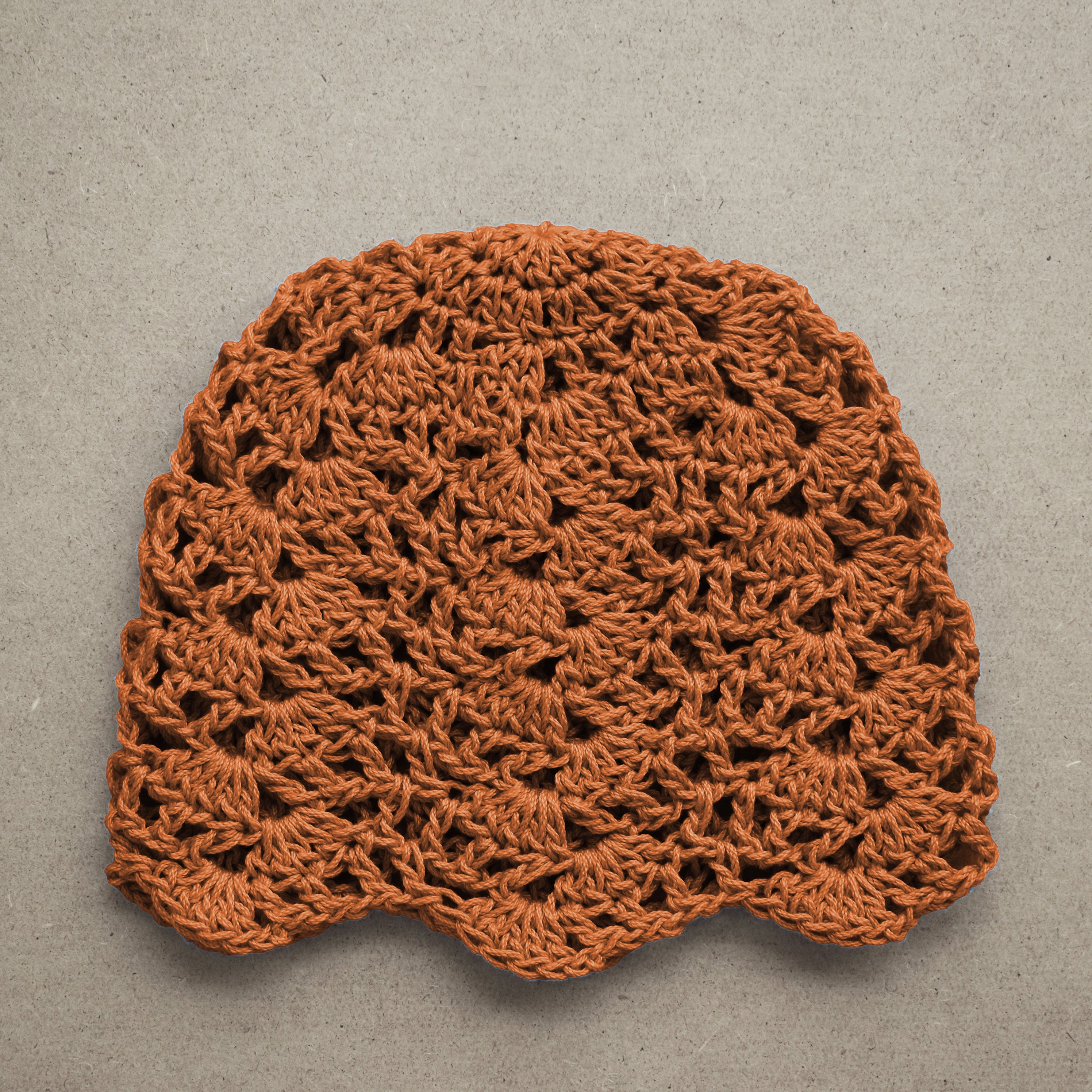 Amber orange crocheted lace beanie on a textured kraft background.