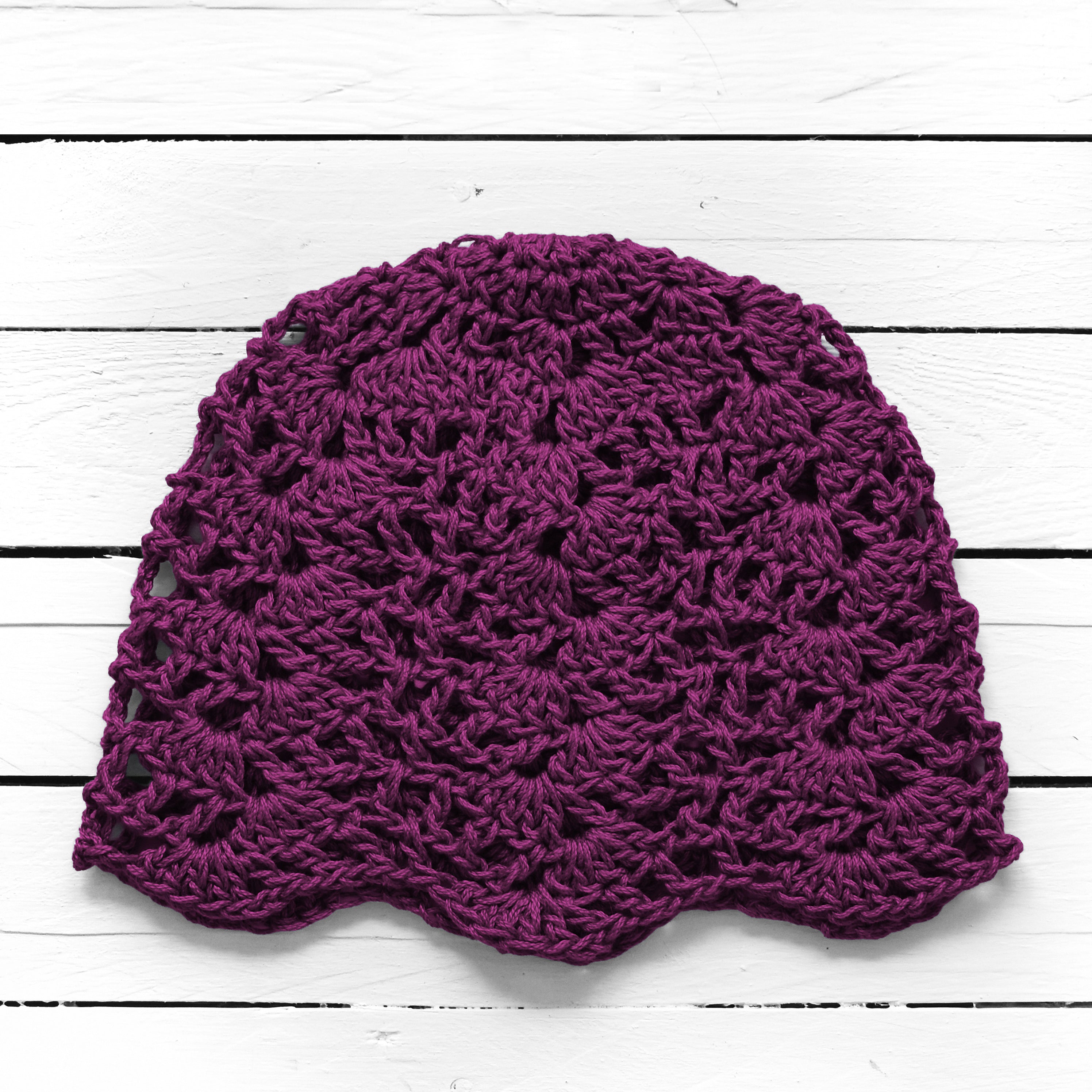 Dark purple crocheted lace skull cap on a white wooden surface.