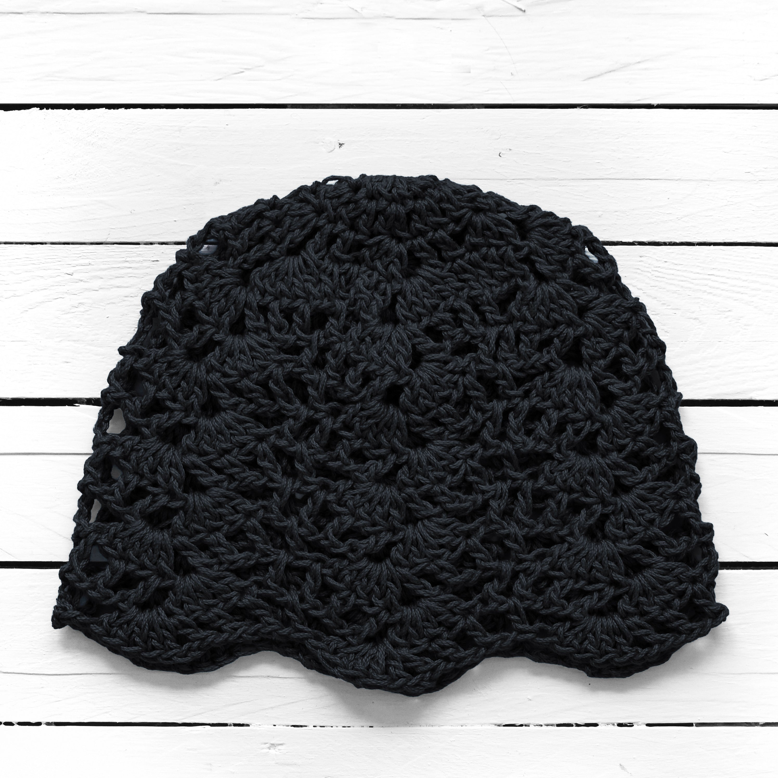 Black crochet lace beanie on a white wooden surface.