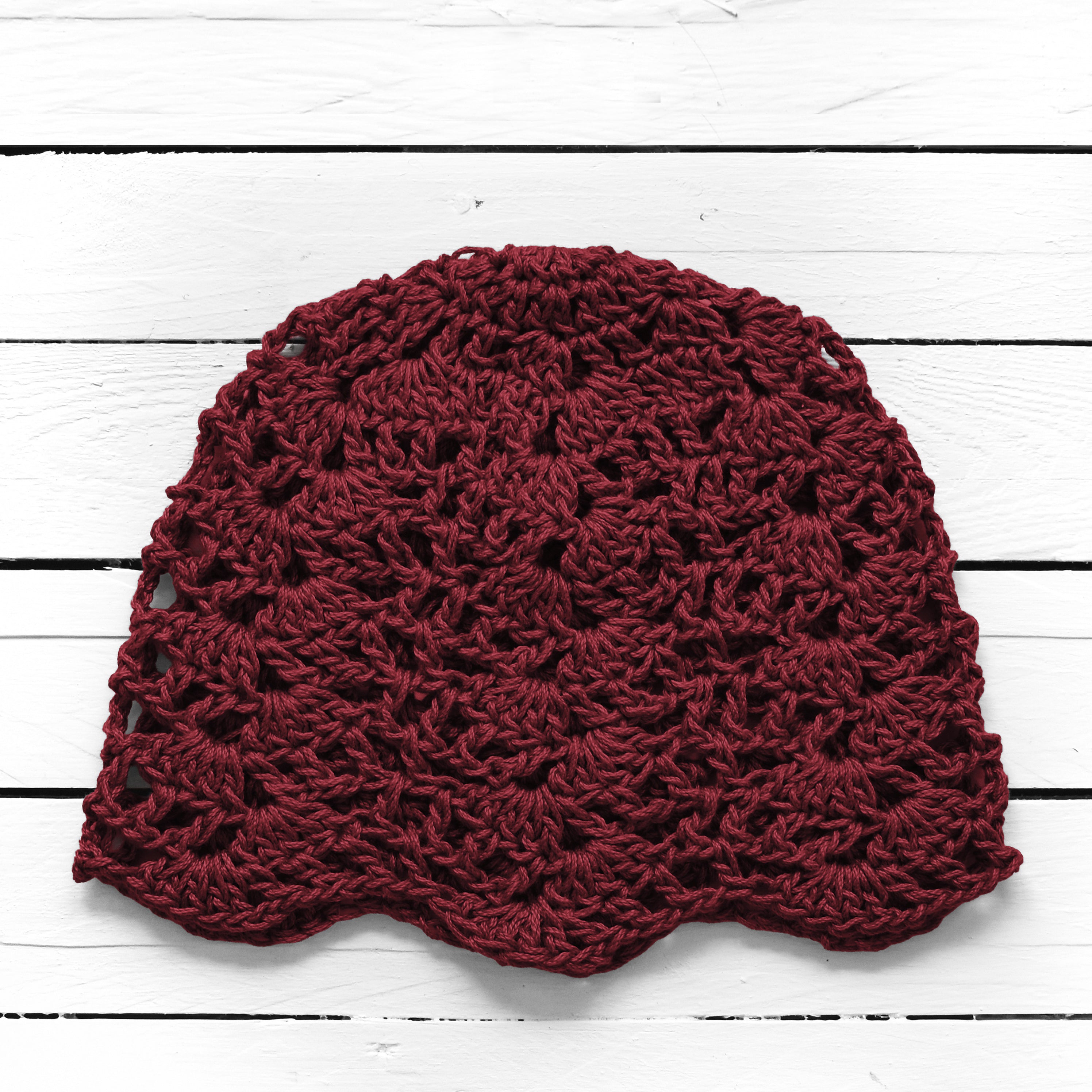 Maroon crocheted beanie on a white wooden surface.