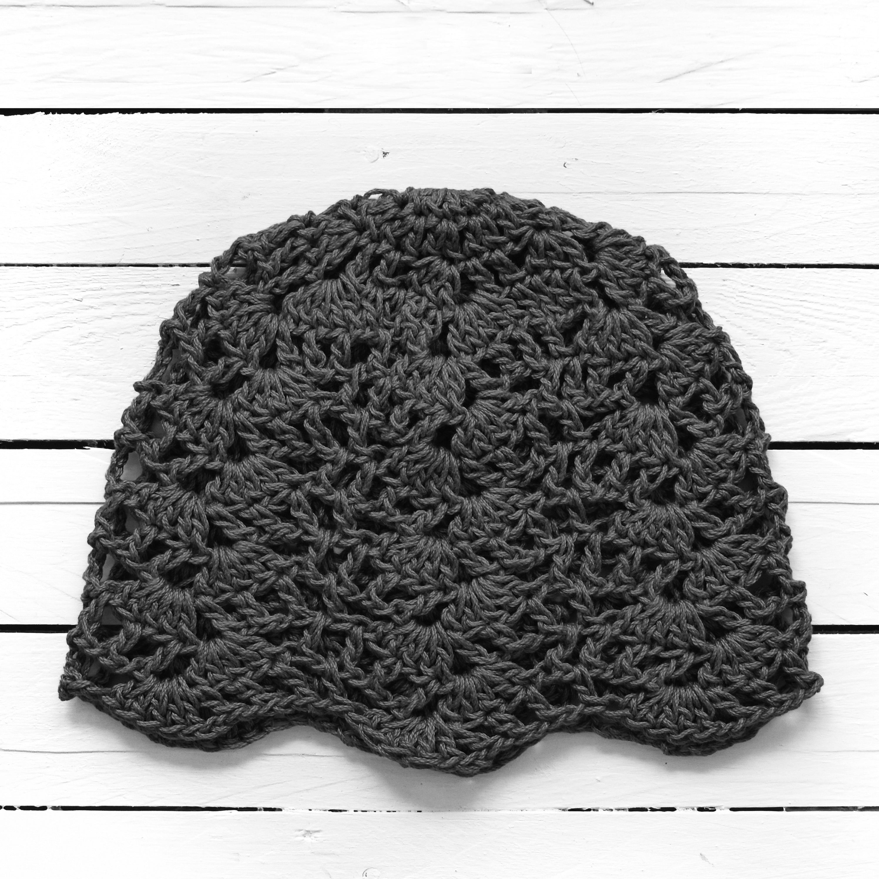 Dark gray crochet lace beanie on a white wooden surface.