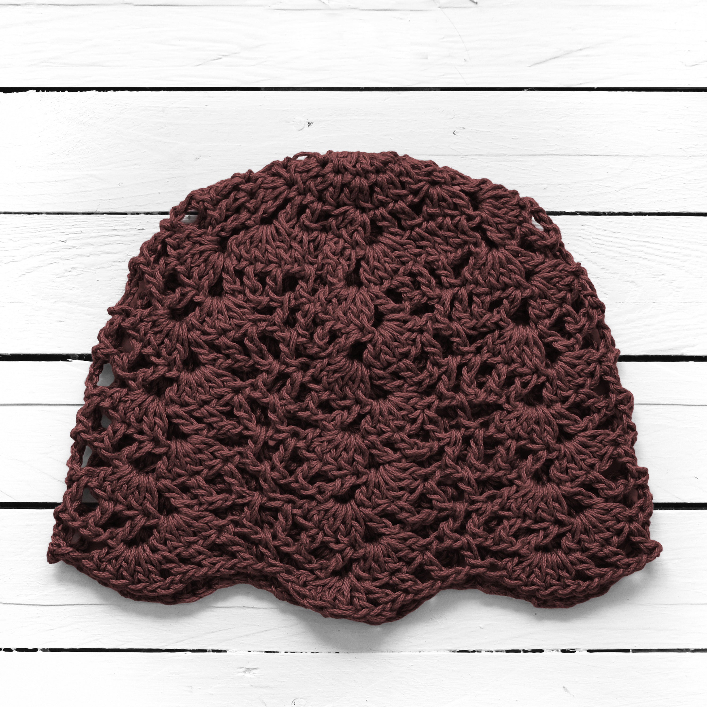 Brown crocheted lace hat on a white wooden surface.