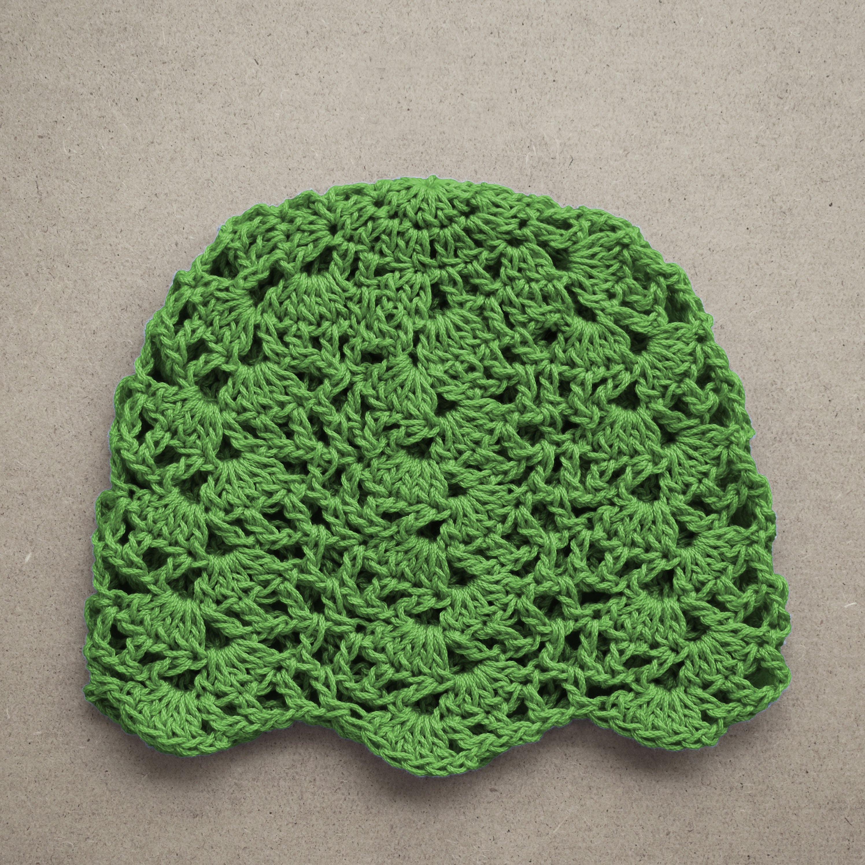 Green crocheted hat on a beige background.