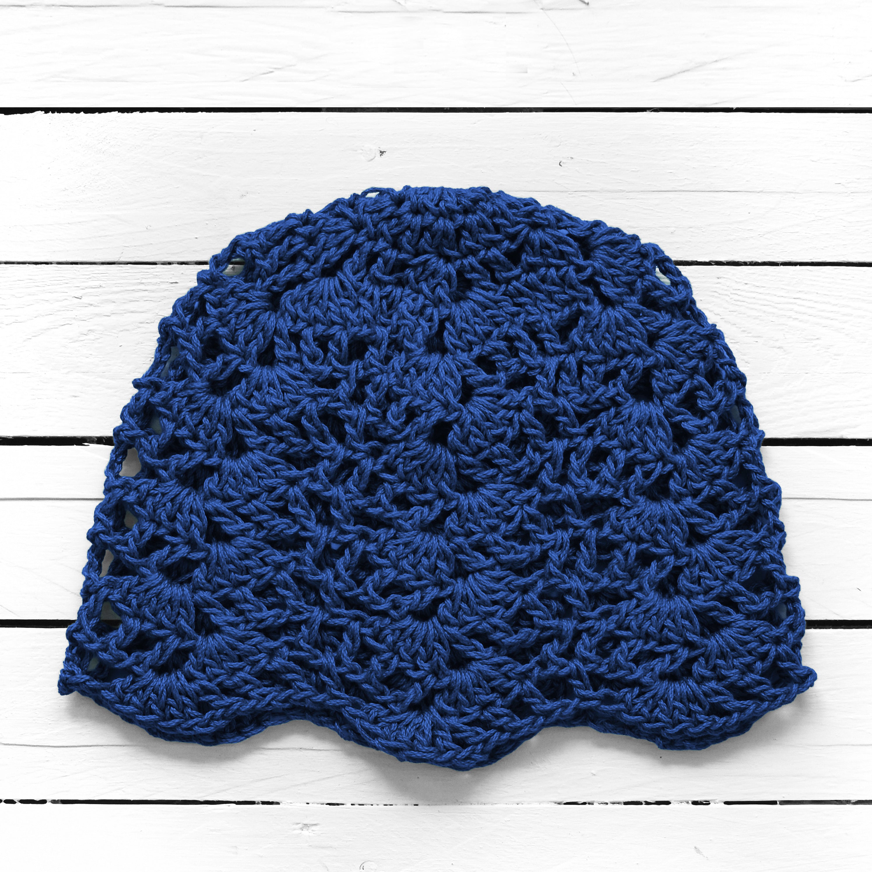 Blue crocheted beanie on a white wooden surface.