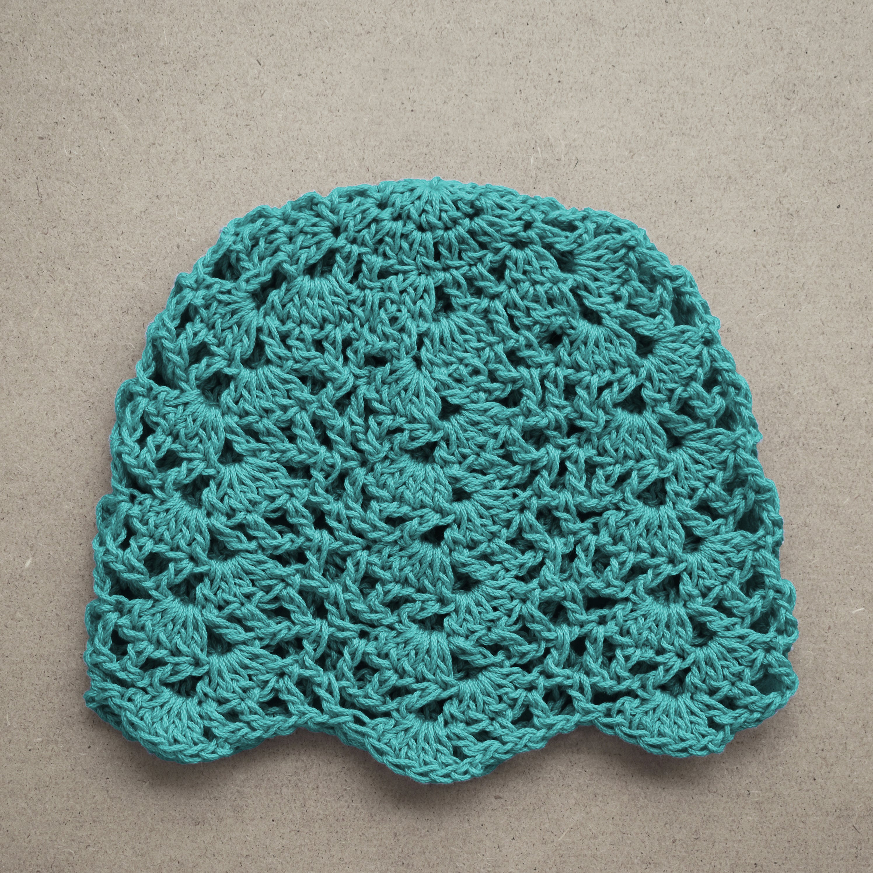 Teal crocheted lace cap on a beige background.