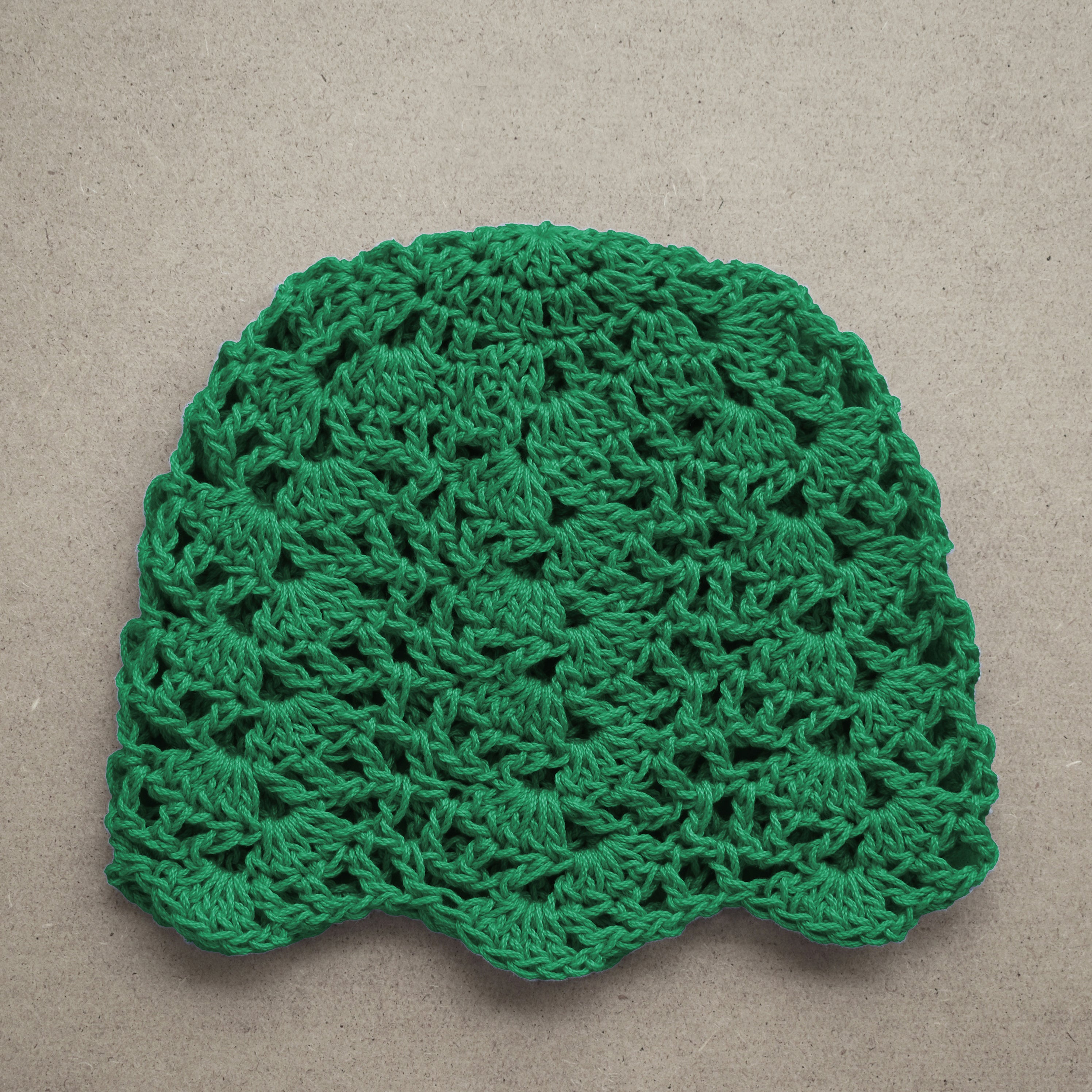 Green crocheted beanie on a beige background.