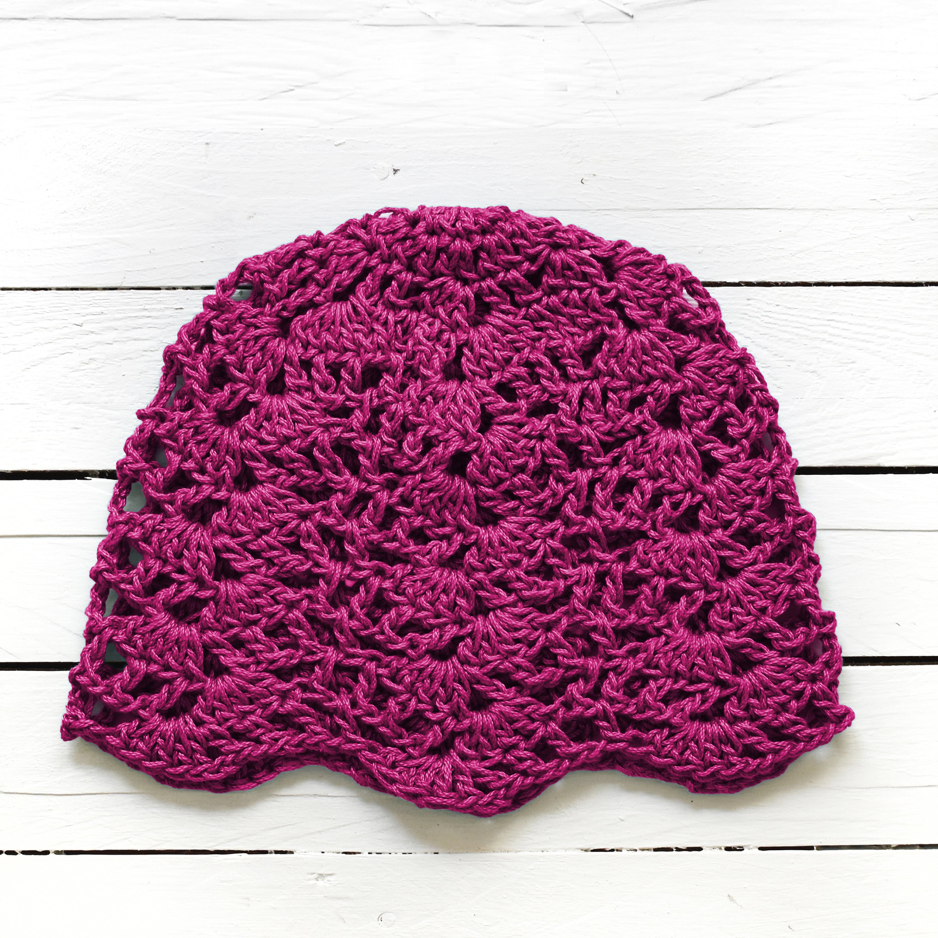 Magenta-pink crocheted lace hat on a white wooden surface.