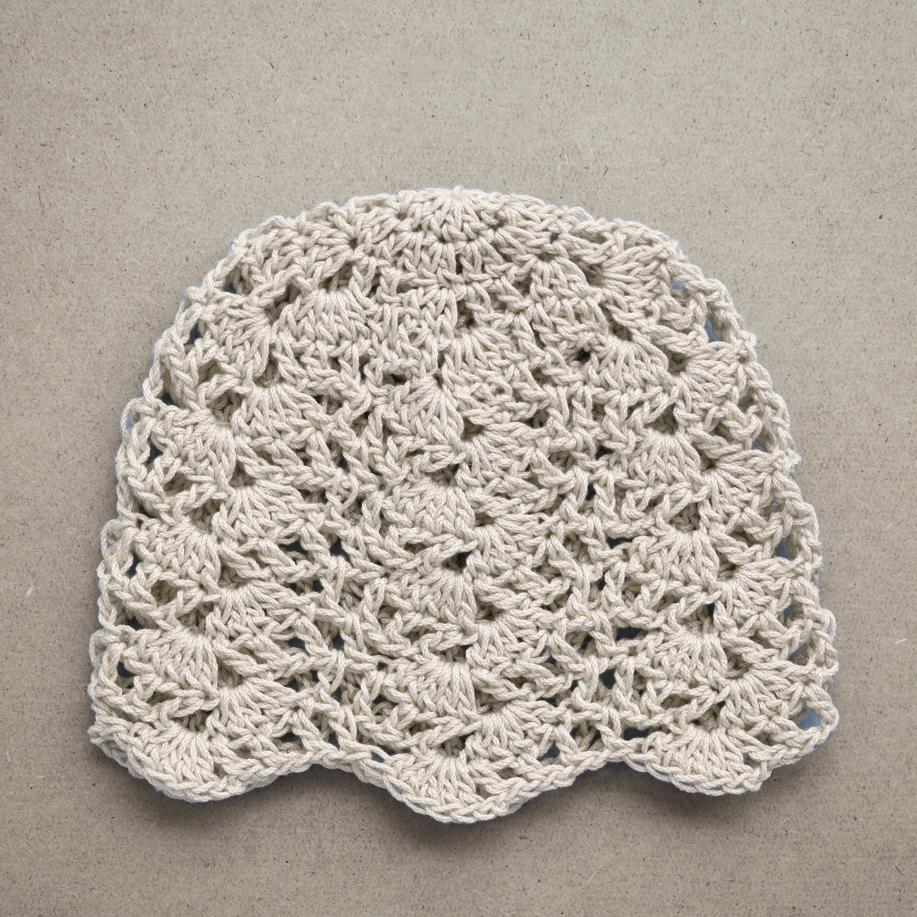 Crocheted beige lace beanie on a textured kraft background.