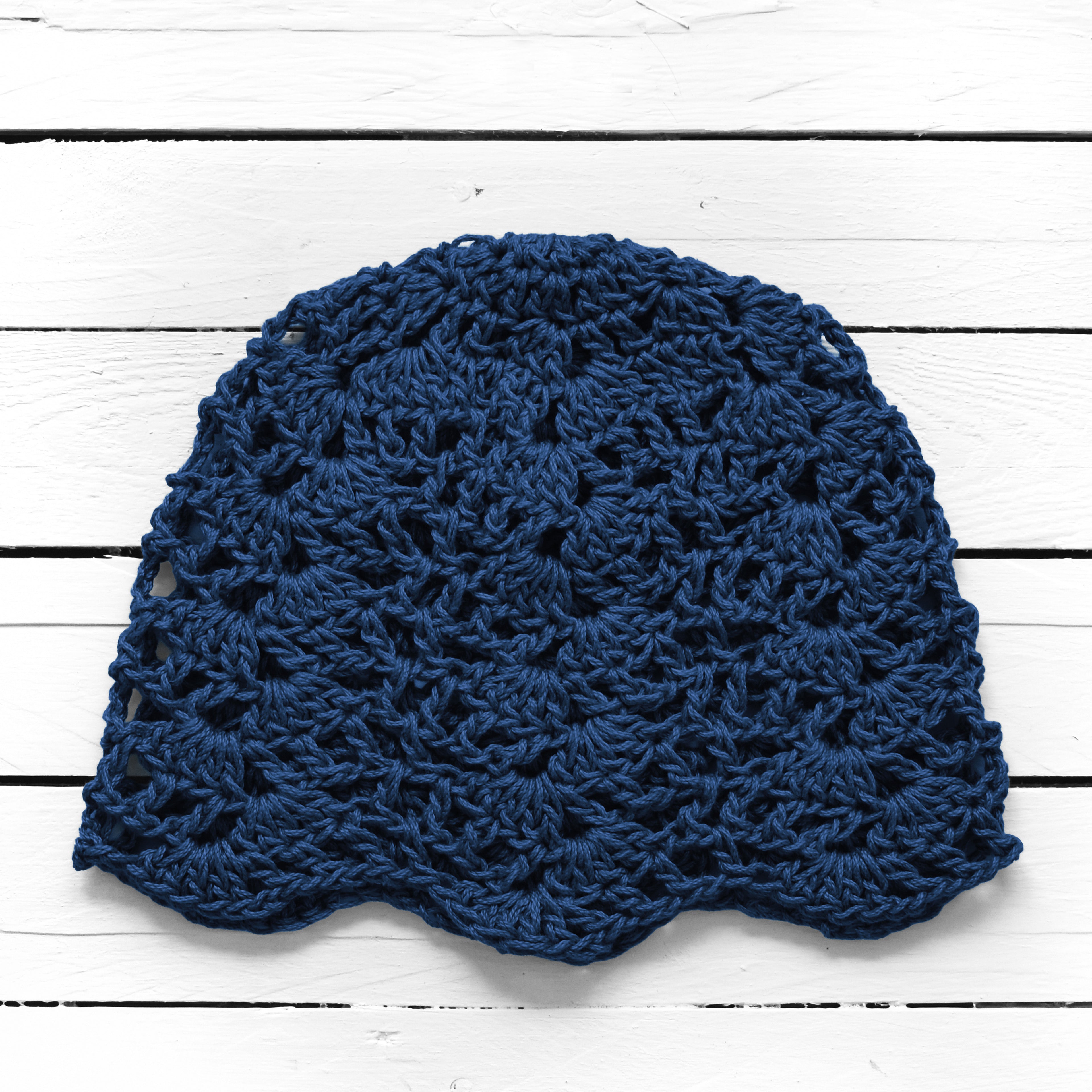 Navy blue crocheted beanie on a white wooden surface.
