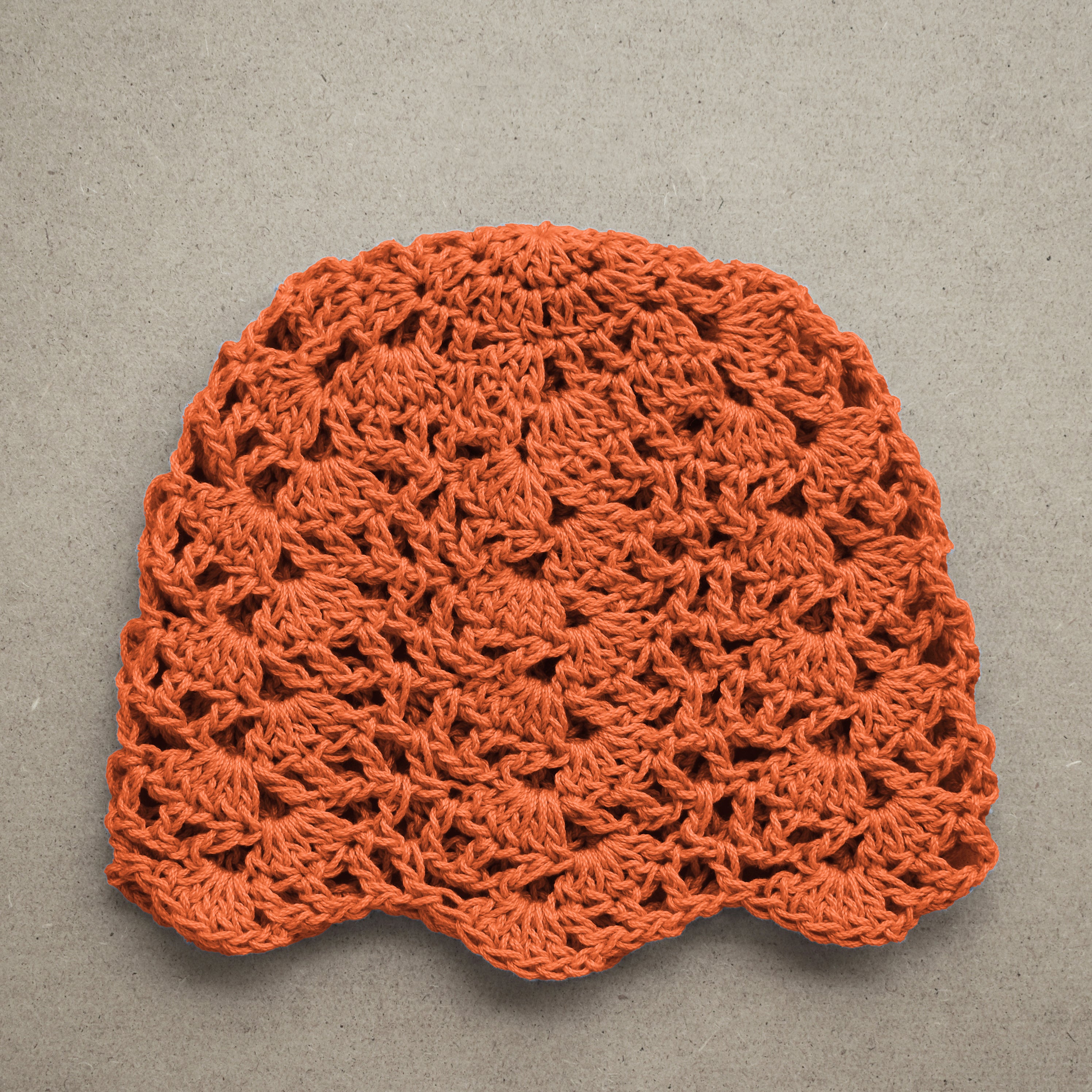 Crocheted orange cap on a textured kraft background.