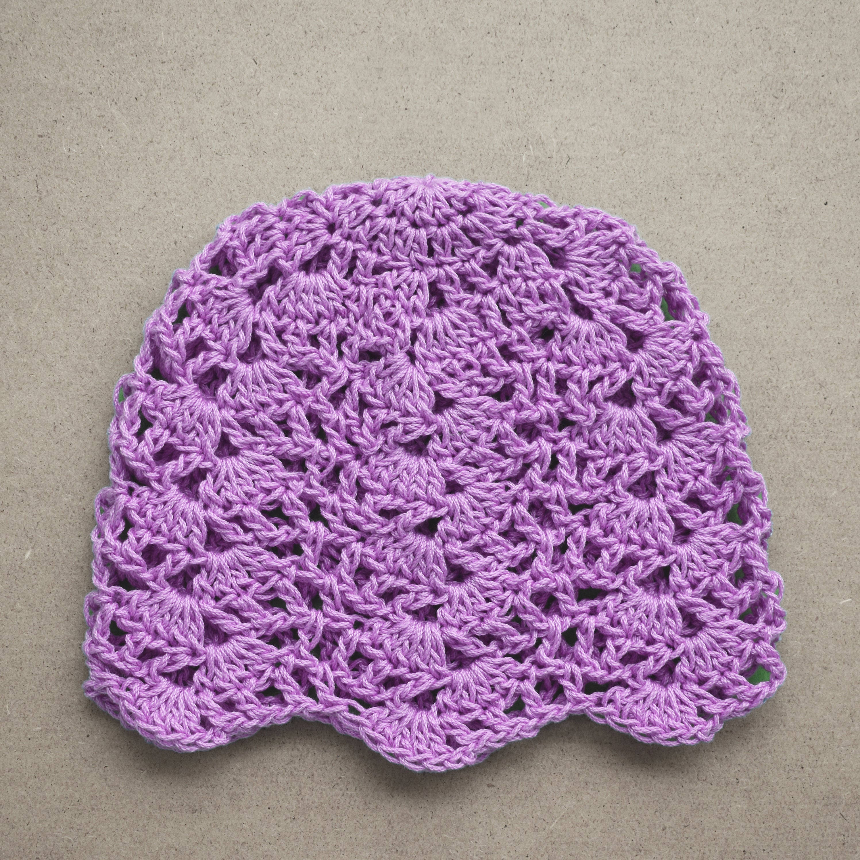 Light purple crocheted lace hat on a beige background.