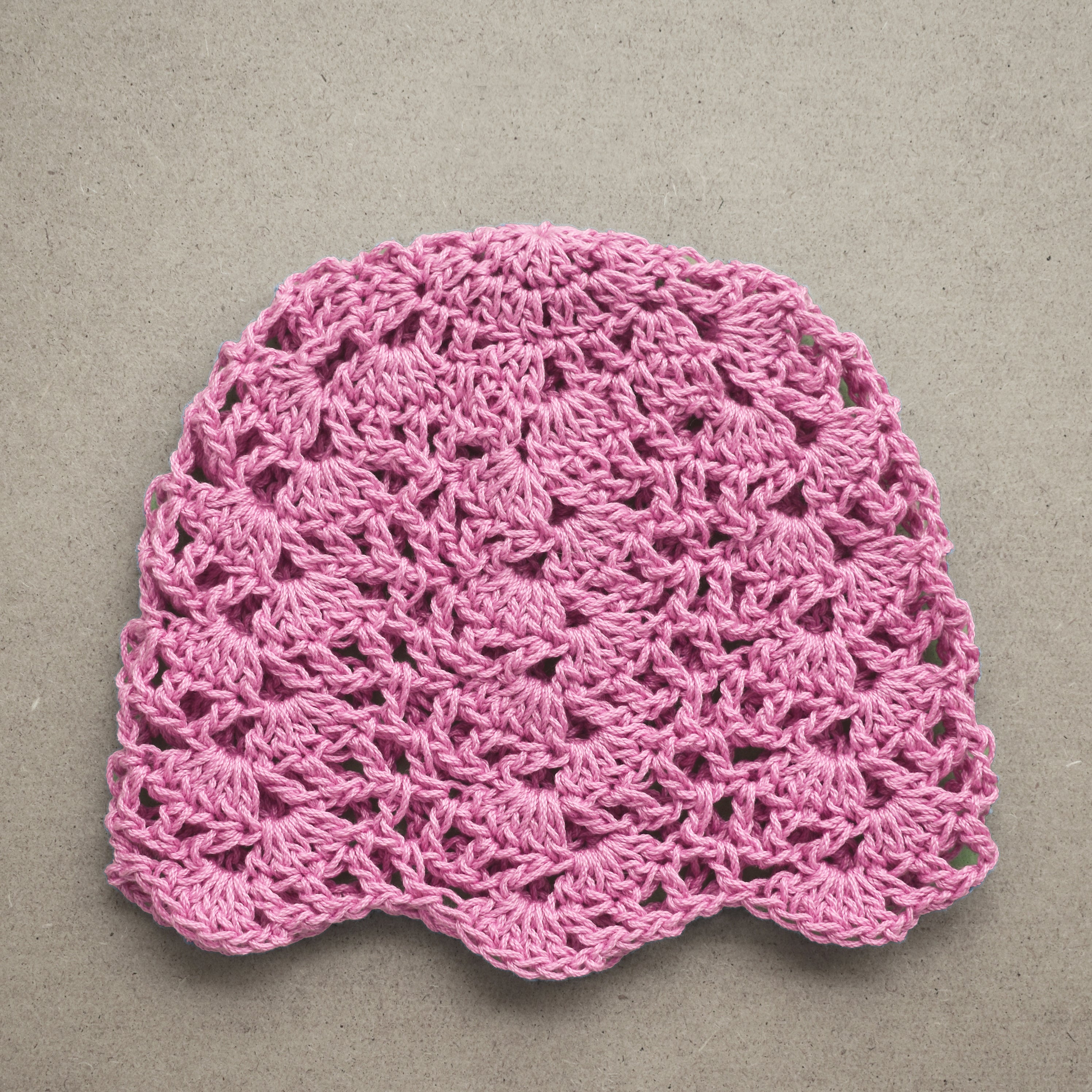 Pink crocheted hat on a textured kraft background.