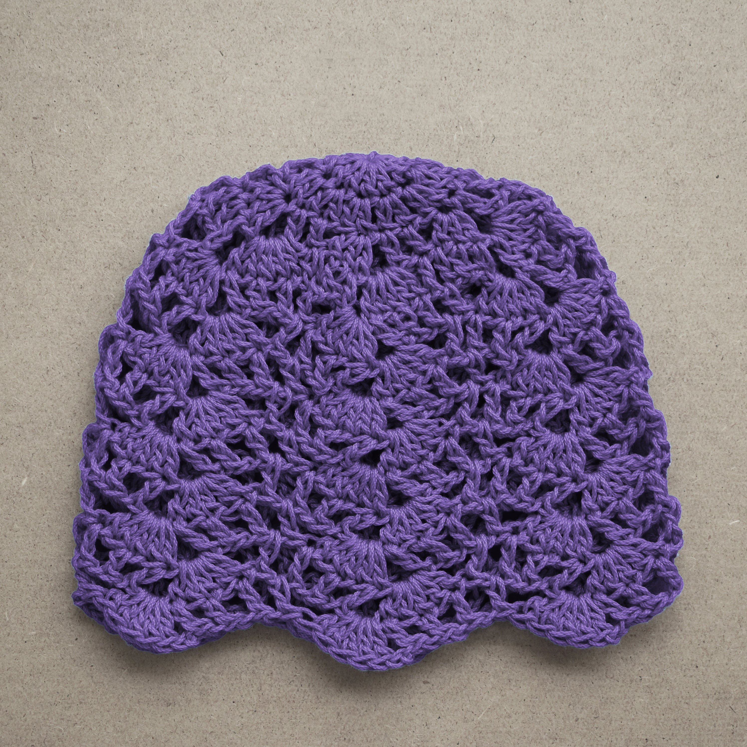 Purple crocheted beanie on a beige background.