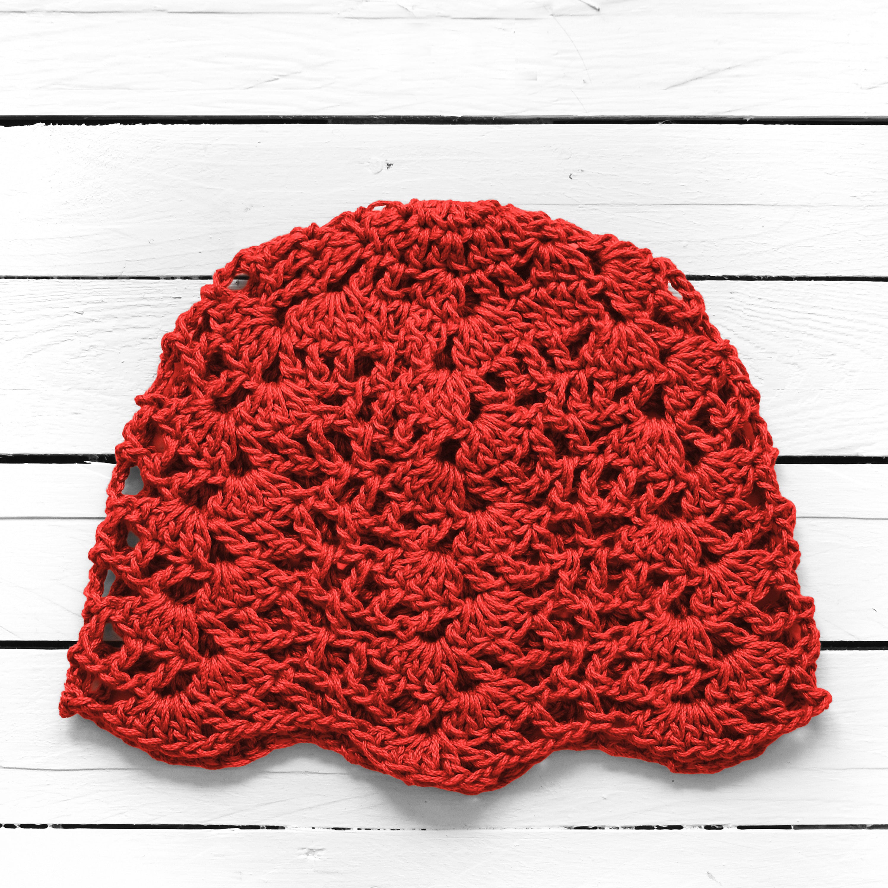 Red crocheted beanie on a white wooden surface.