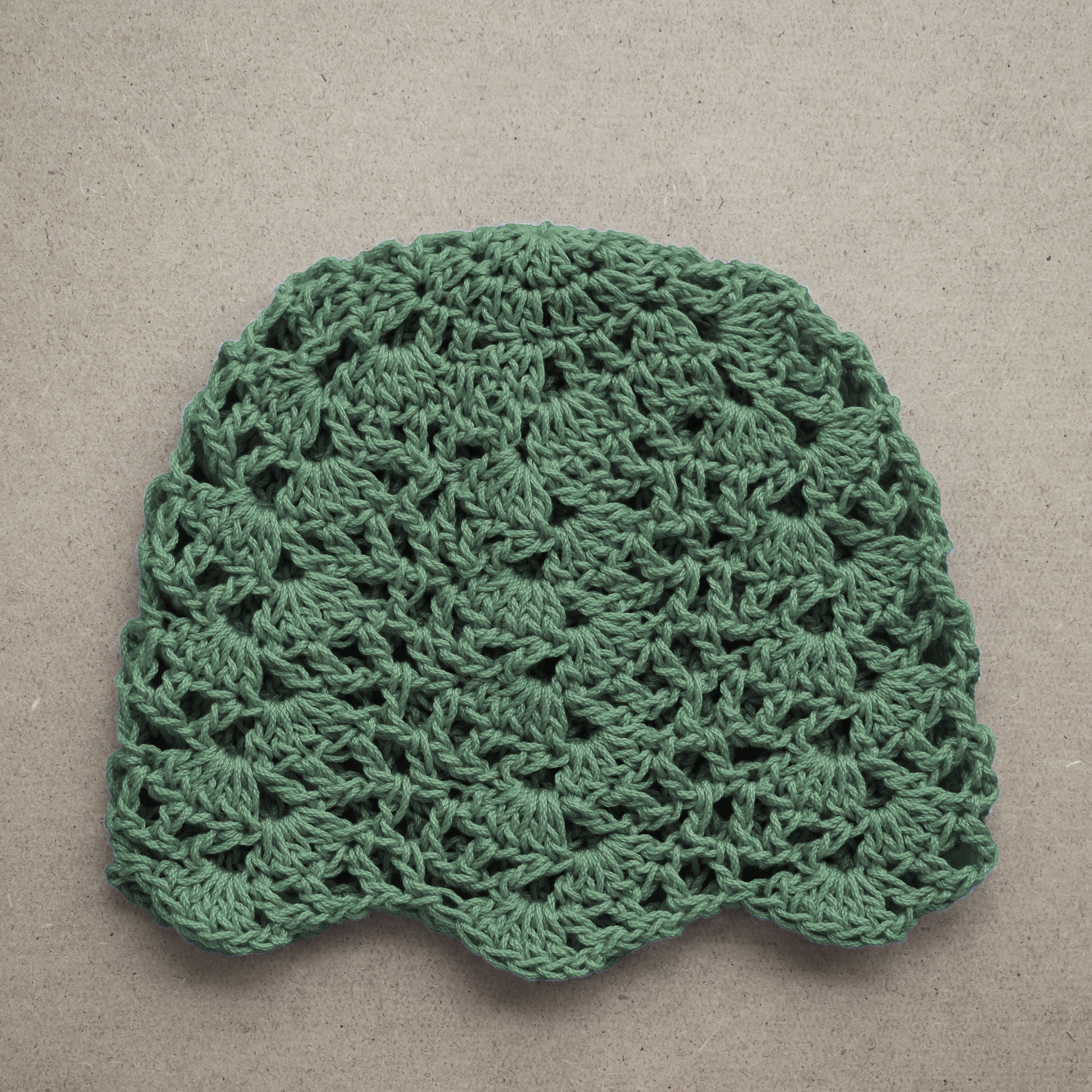 Green crocheted lace beanie on a beige background.