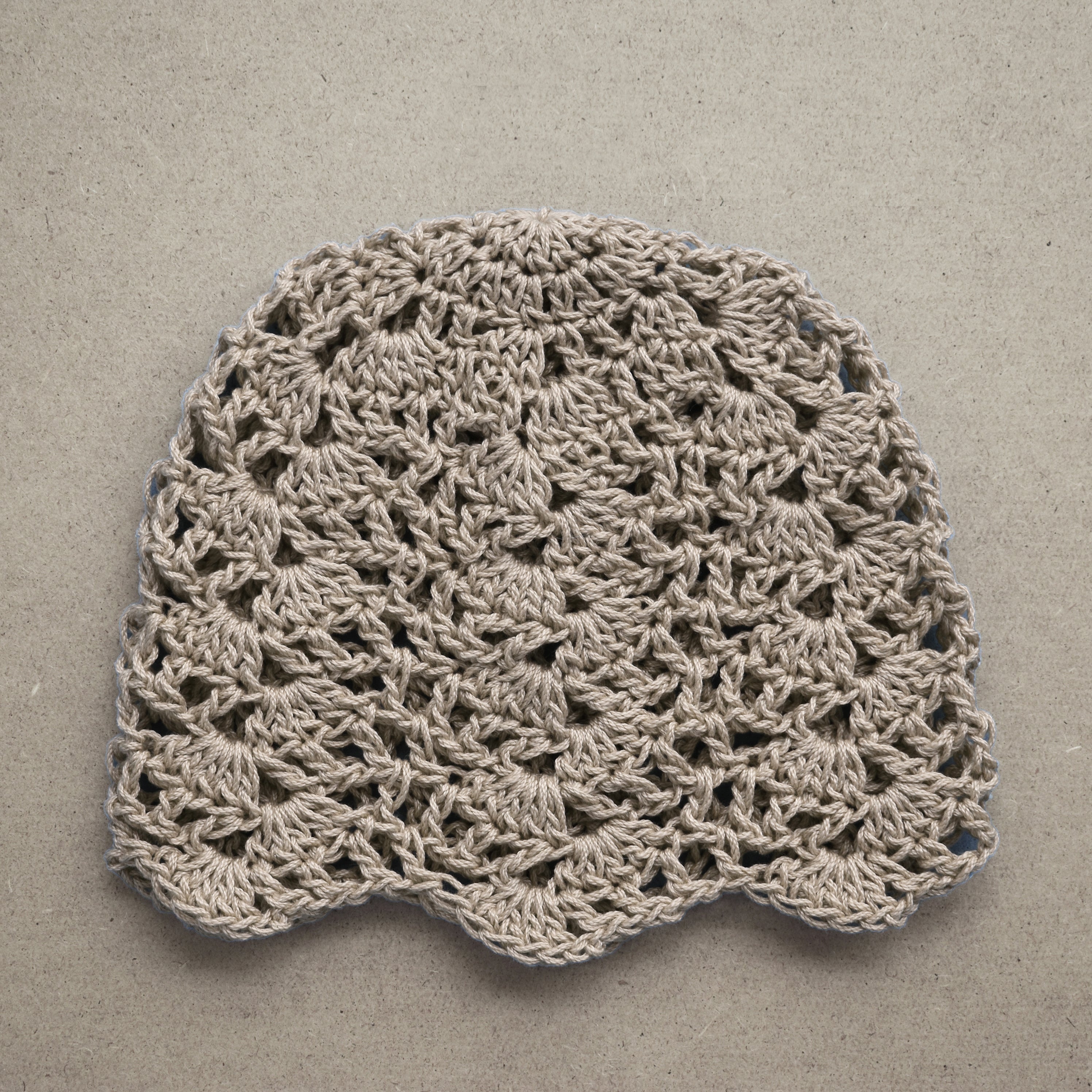 Crocheted lace taupe hat on a textured beige background.