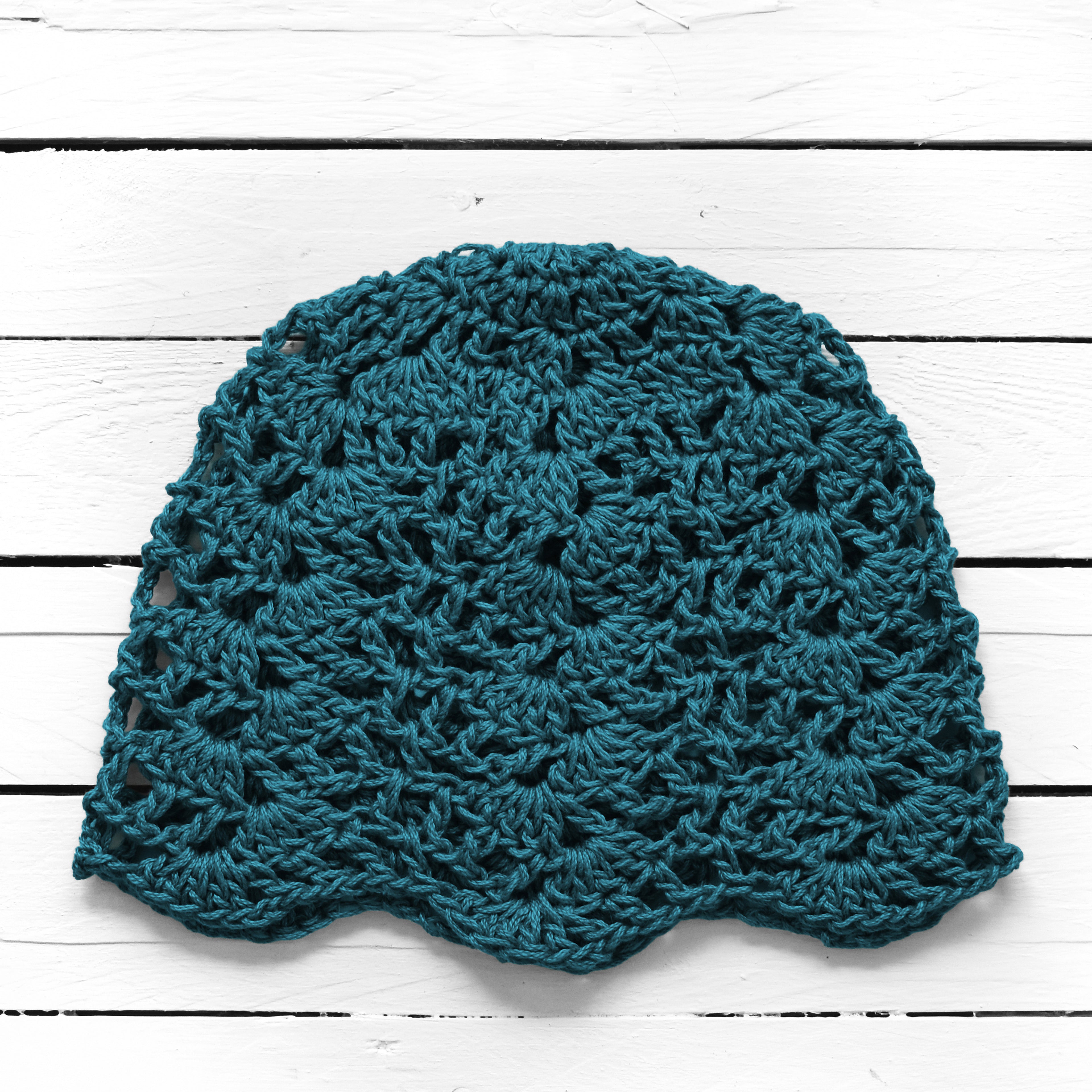 Teal crocheted lace summer hat on a white wooden surface.