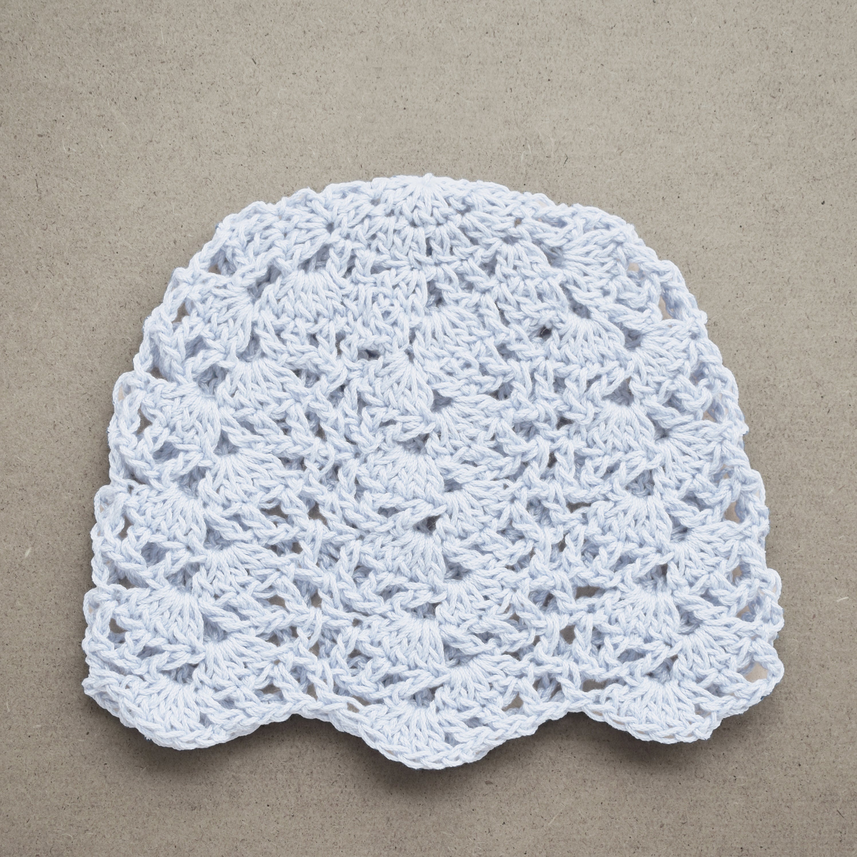 White crocheted hat on a textured brown background.