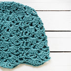 Teal crocheted hat on a white wooden surface.