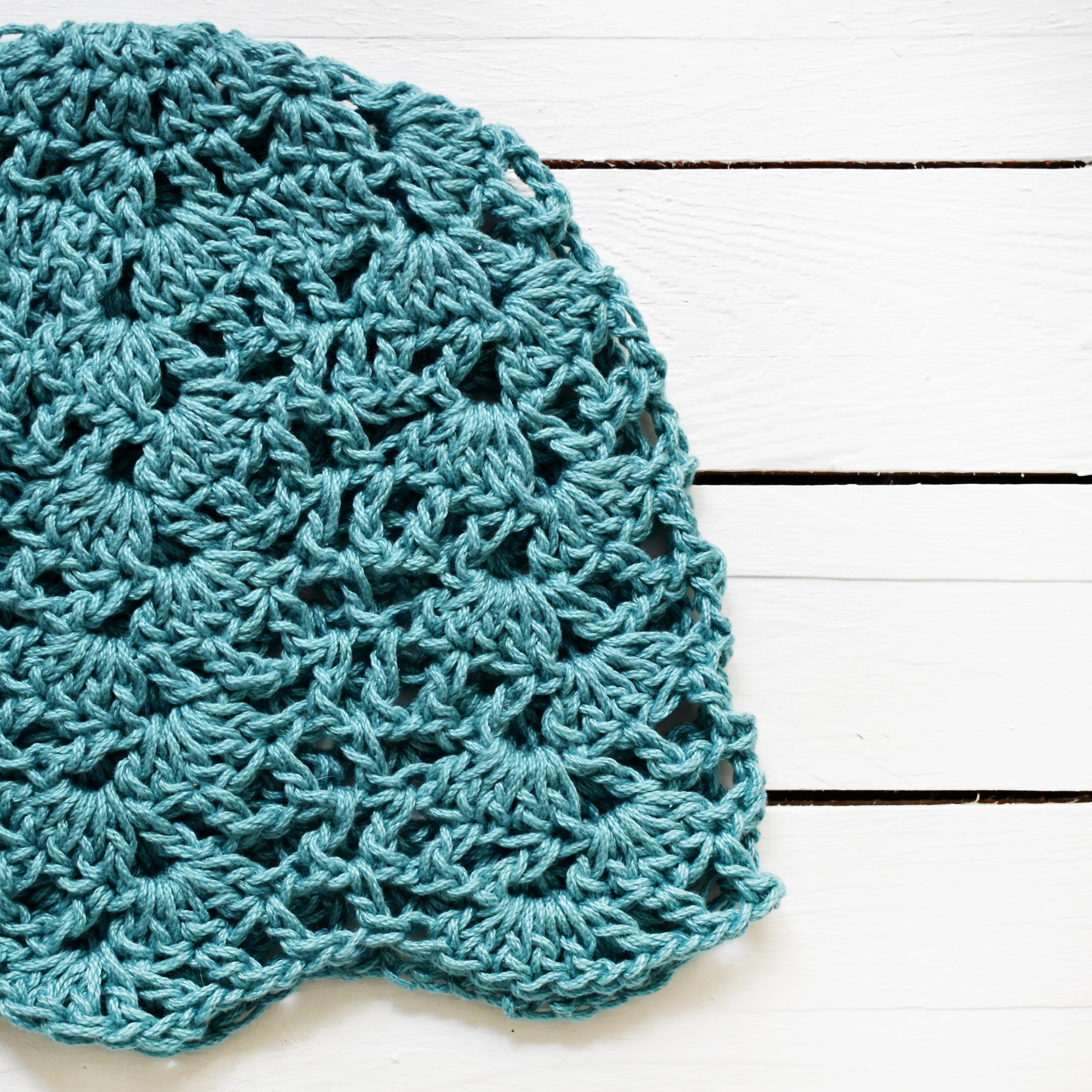 Teal crocheted hat on a white wooden surface.