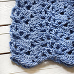 Close-up of a blue crocheted cap on a white wooden surface.