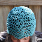 Teal crochet hat worn by a person looking down against a wooden background.