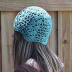 Person wearing a teal crochet hat against a wooden fence background.