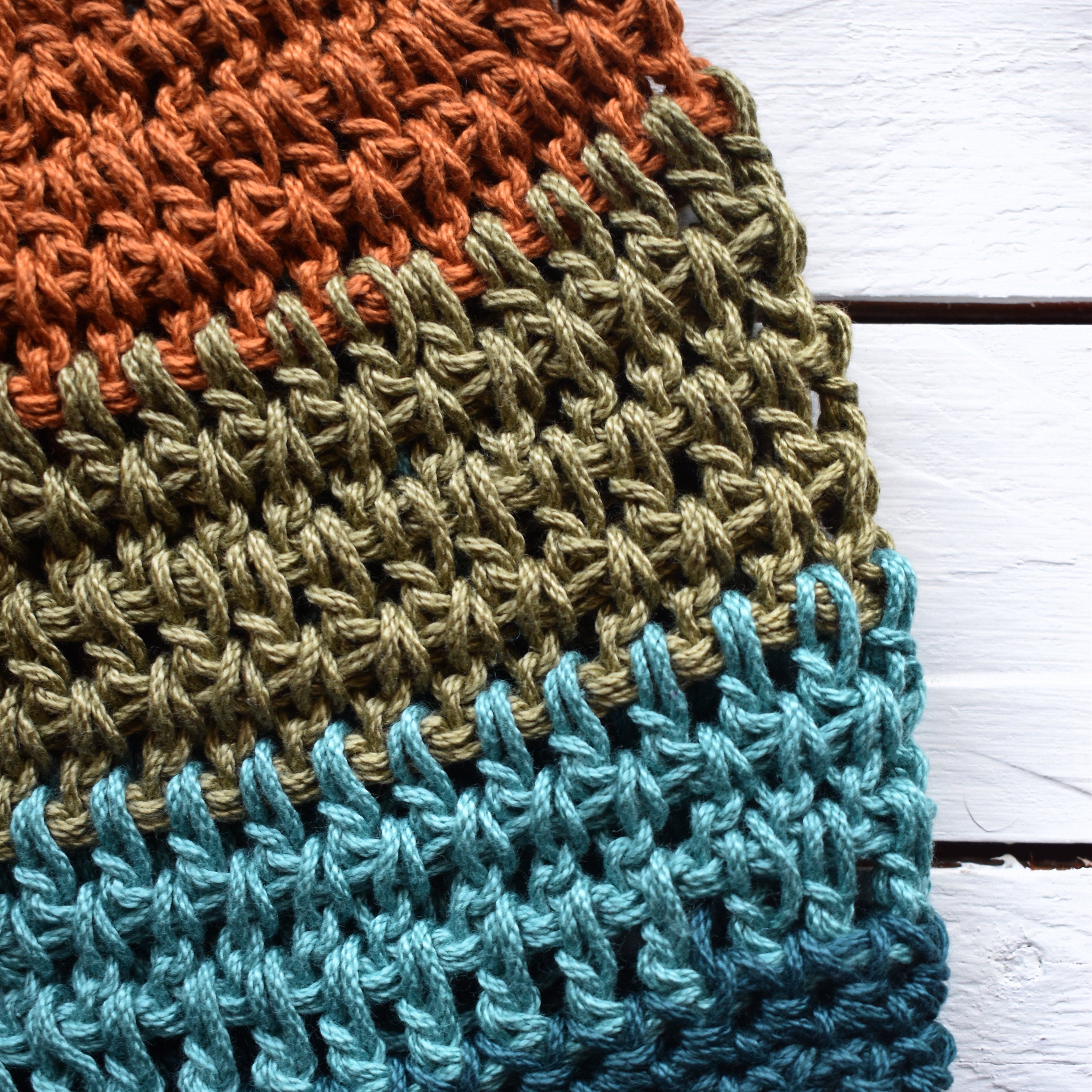 Close-up of a crocheted hat with orange, green, and teal blue stripes on a wooden surface.