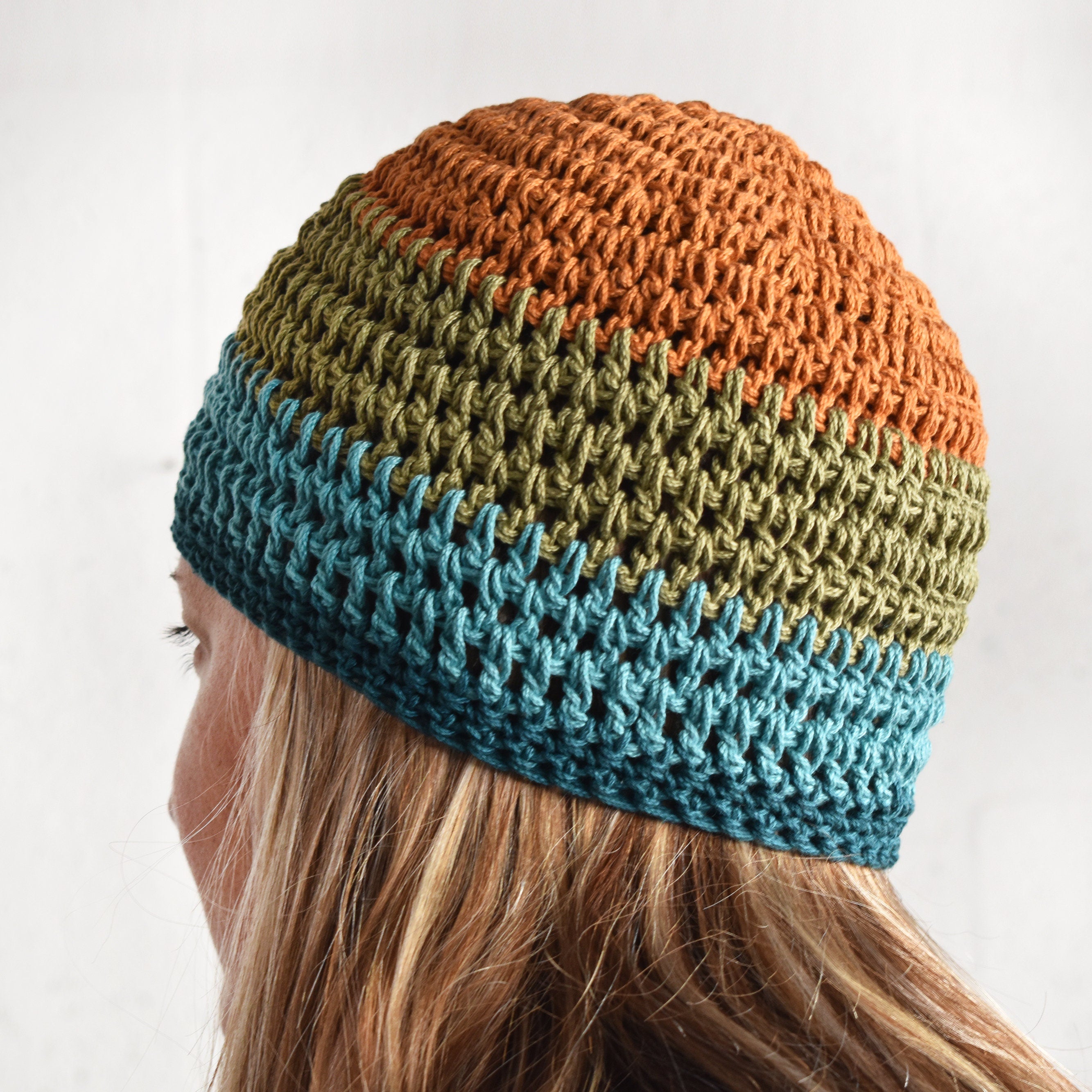 Person wearing a multicolor beanie against a nuetral colored background.
