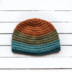 Crocheted beanie with orange, green, and teal blue stripes on a white wooden surface.