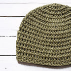 Green crochet beanie on a white wooden surface.