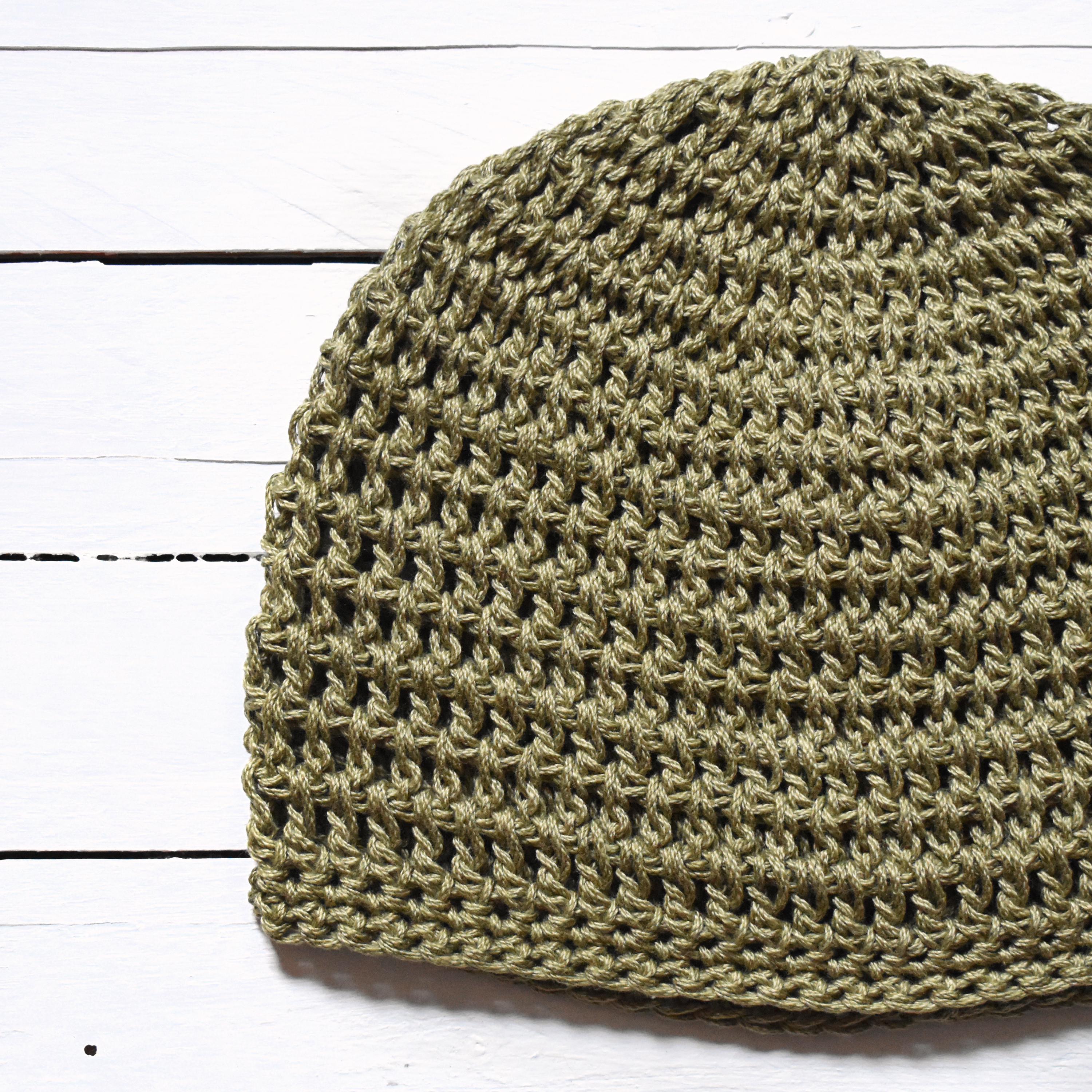 Green crochet beanie on a white wooden surface.