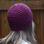 Person wearing a purple knitted beanie with a wooden fence background.
